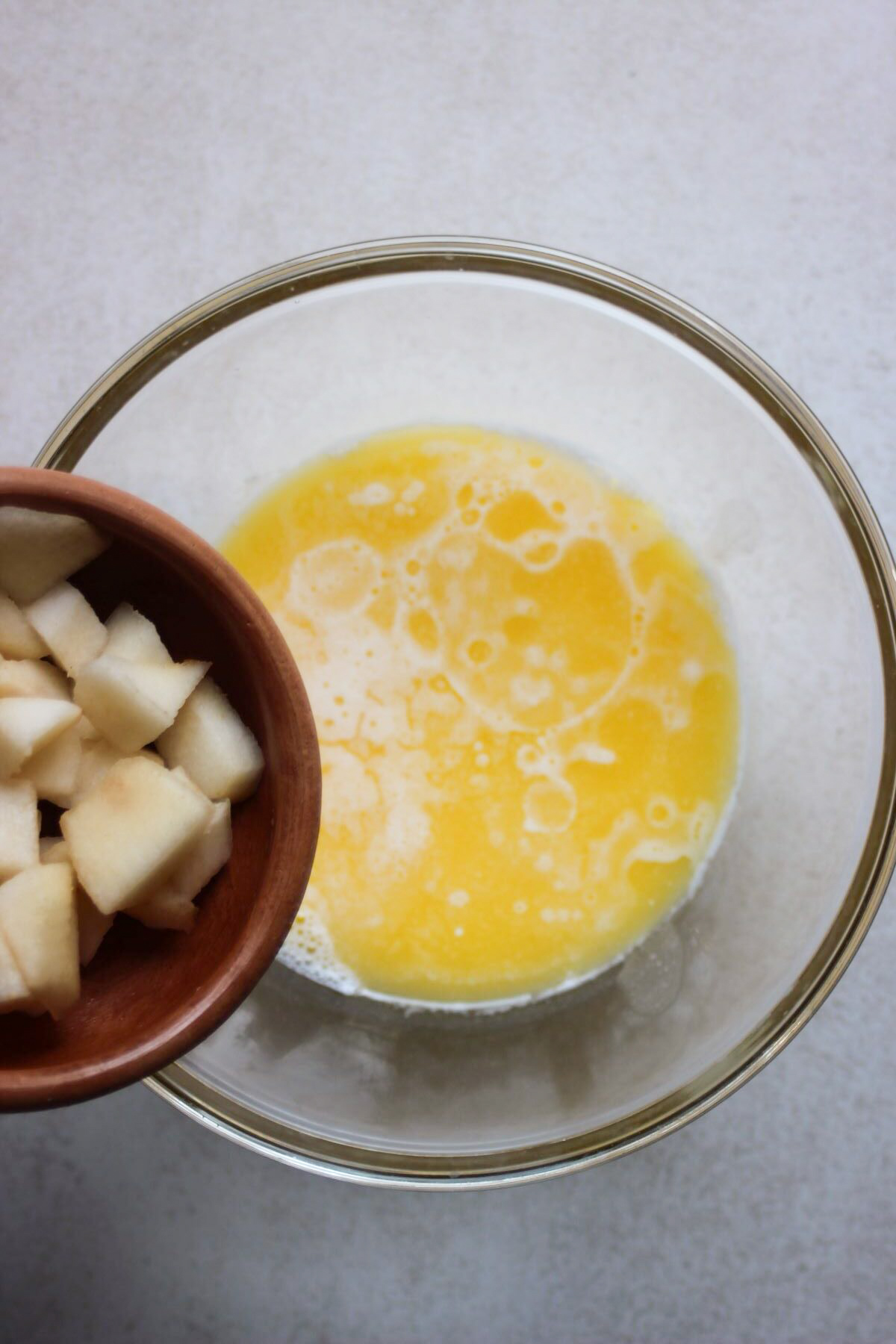Bowl with chopped pears is about to be poured into a glass bowl with a yellow liquid.