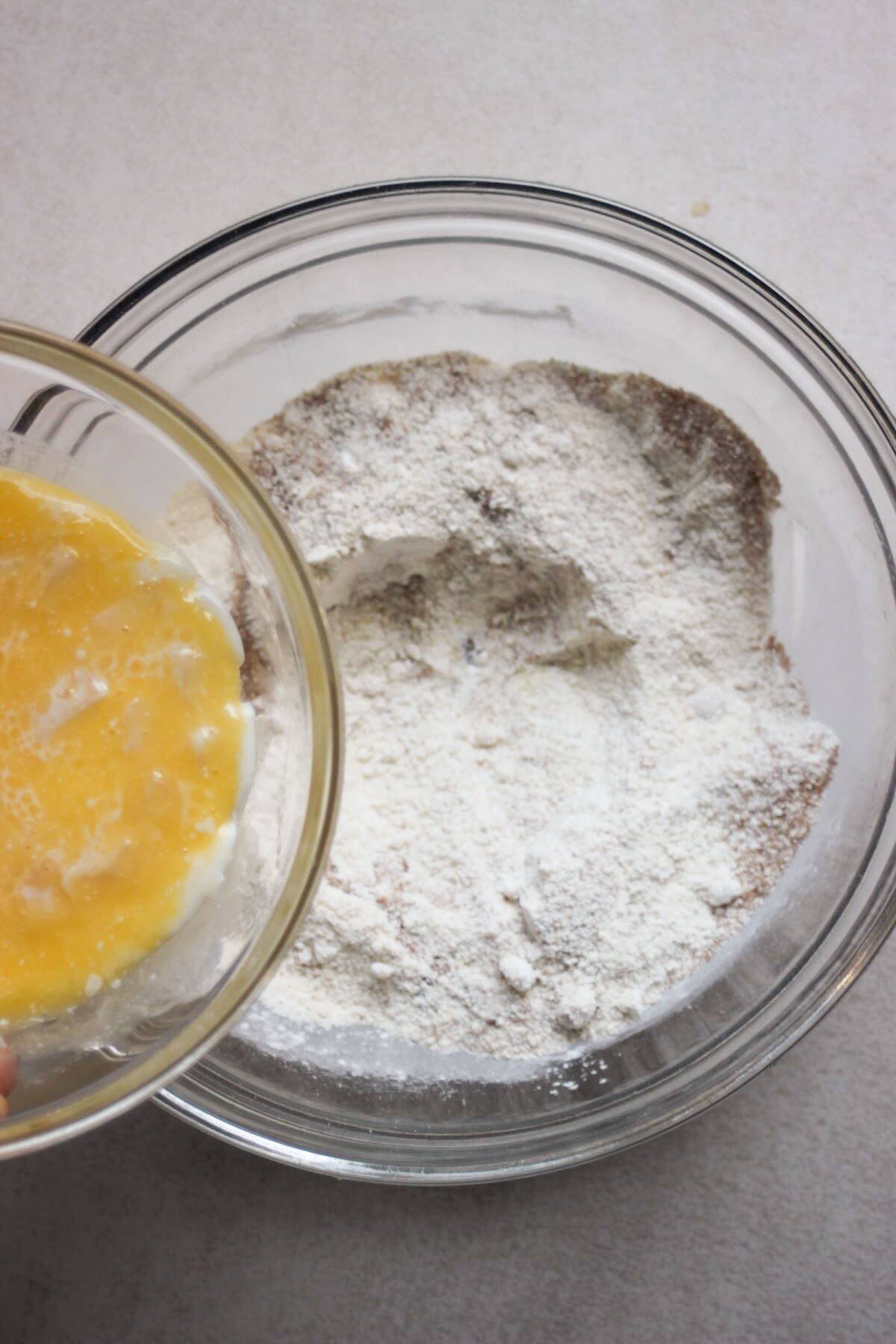 Bowl with a yellow liquid is about to be poured into a bowl with dry ingredients..