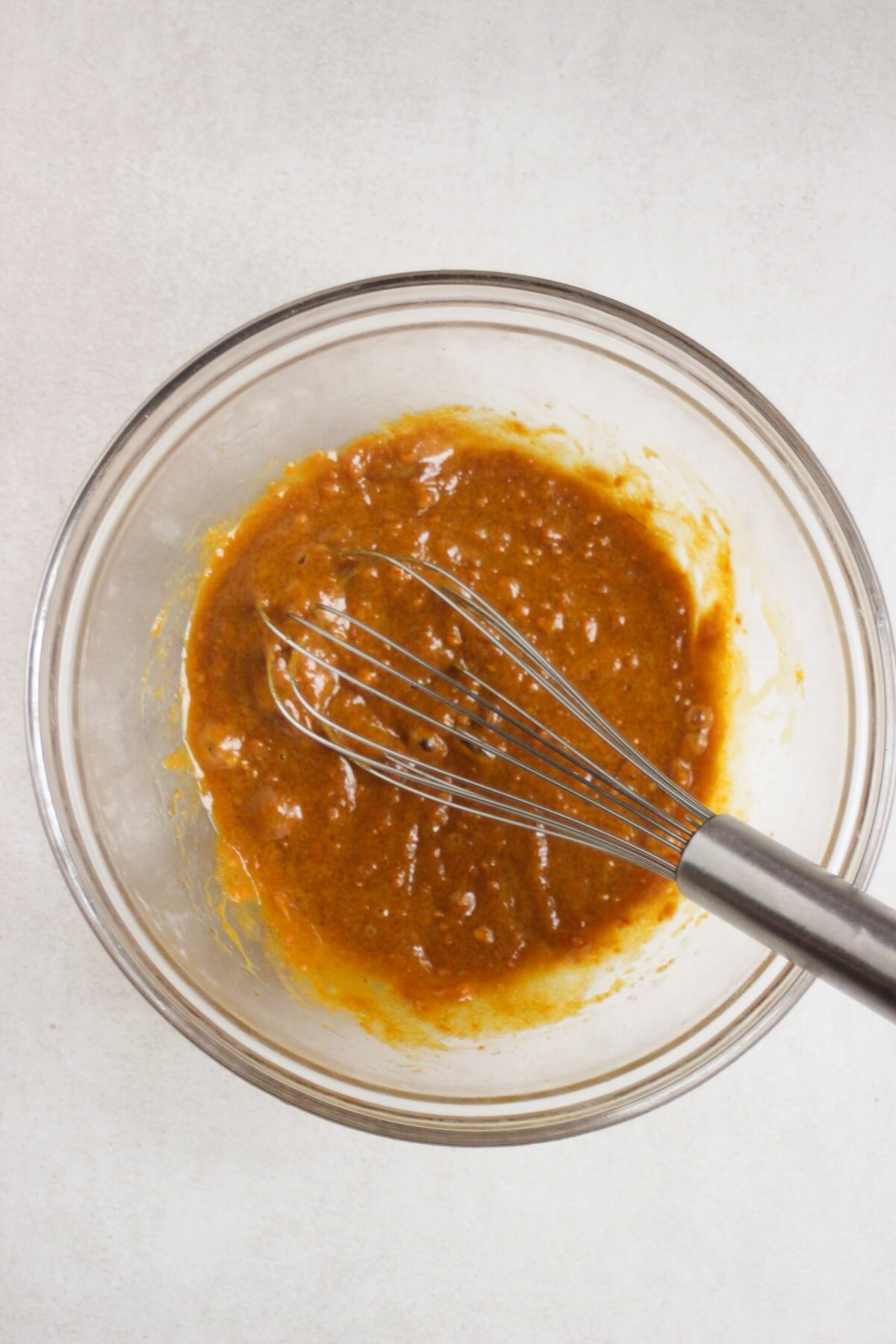 Glass bowl with an orange mixture and a hand whisk.