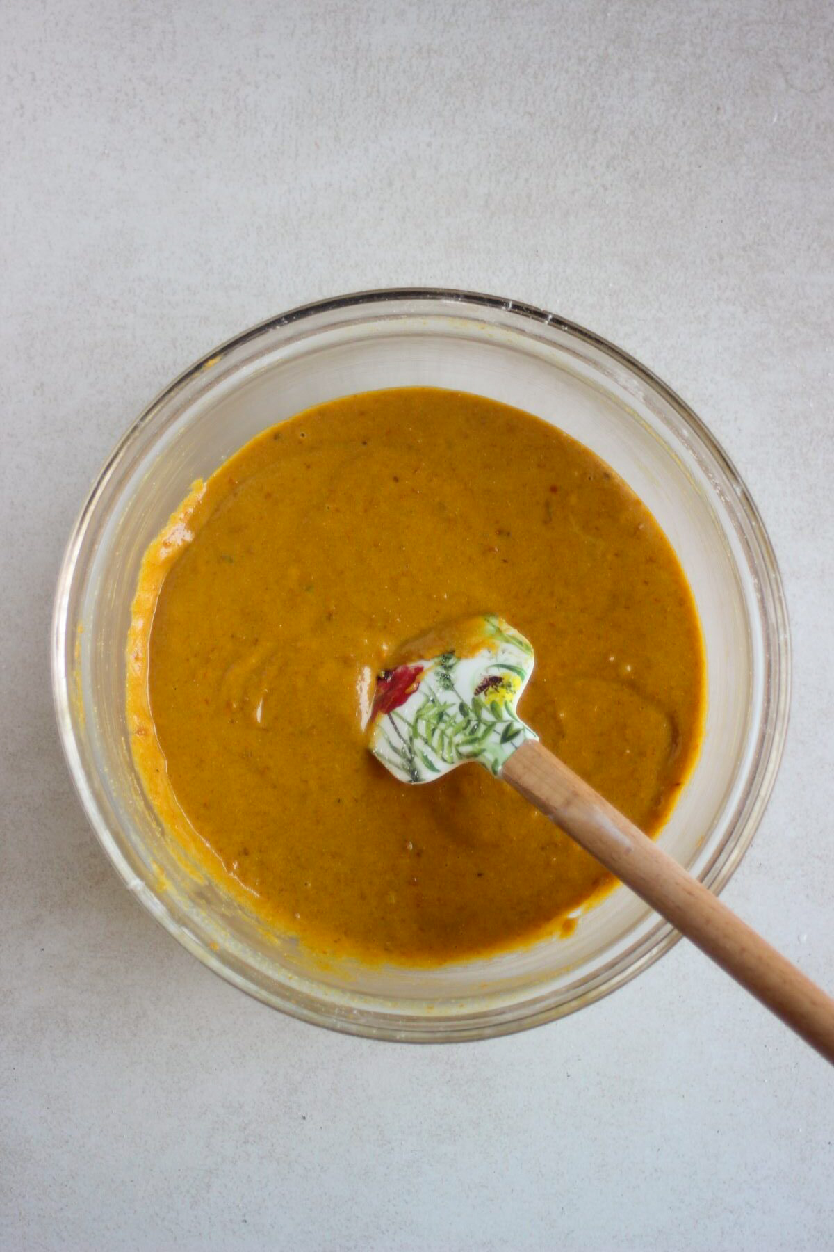 Glass bowl with a smooth orange mixture and a rubber spatula.