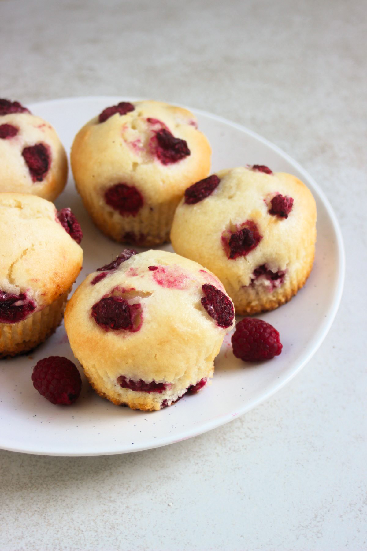 Raspberrie muffins and fresh raspberries on a white plate.