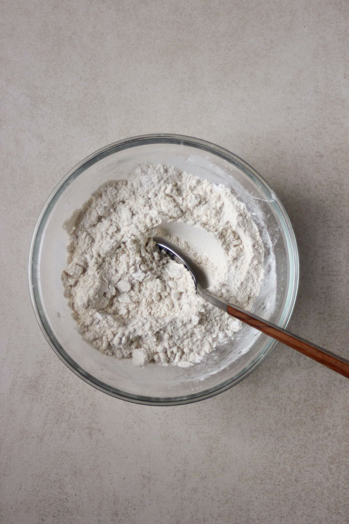 Glass bowl with flour and a spoon.