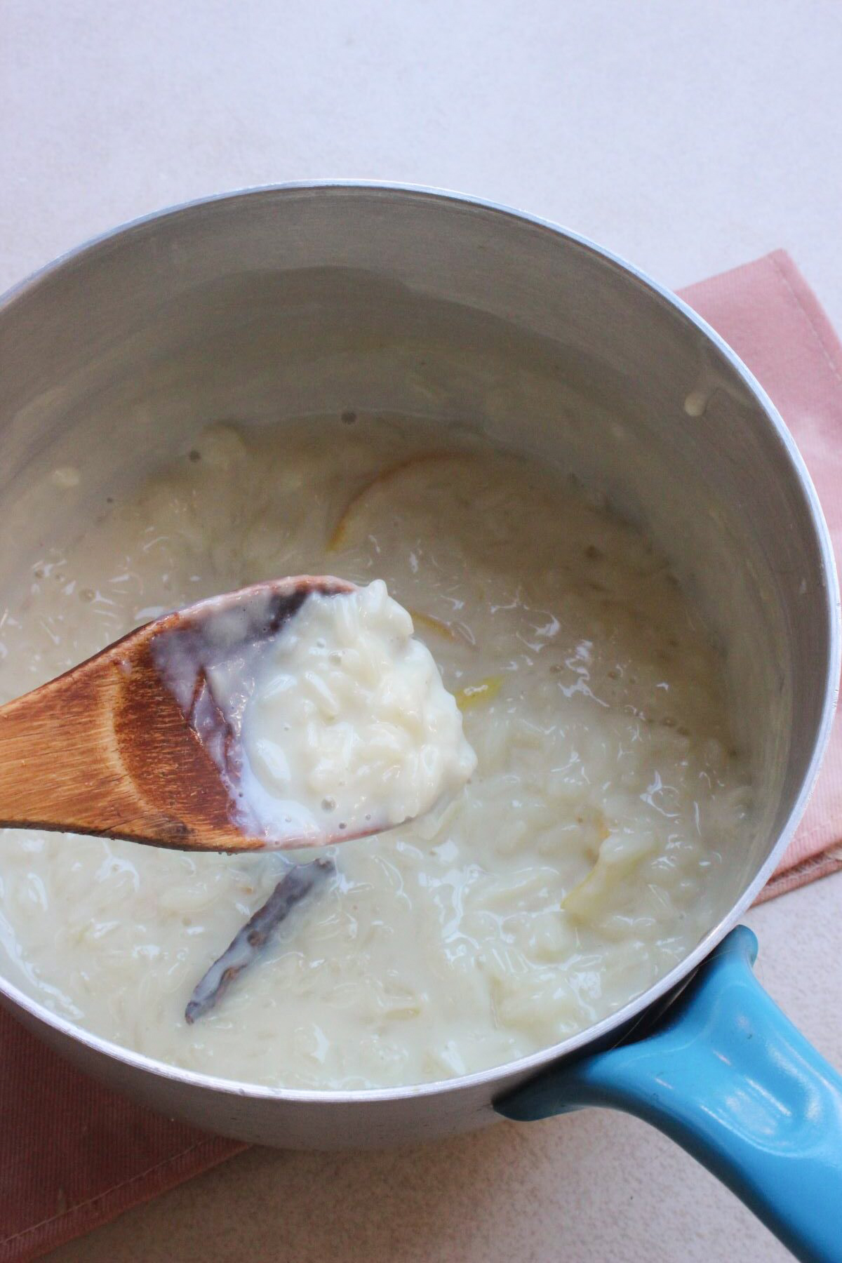 A wooden spoon with rice pudding seen from above. A deep saucepan with rice pudding behind the spoon.