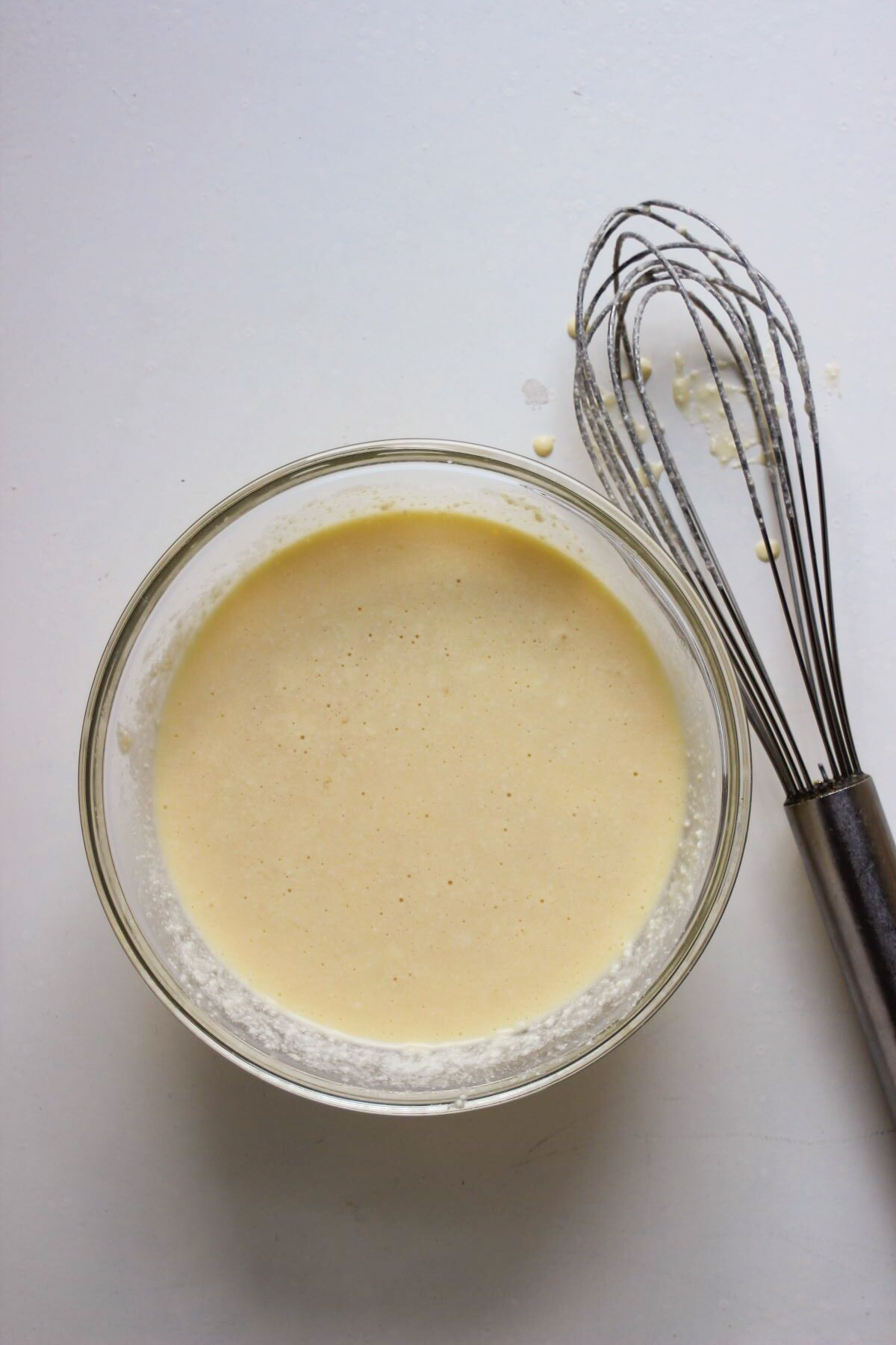 Glass bowl with a cream colour mixture. A hand whisk on the side.