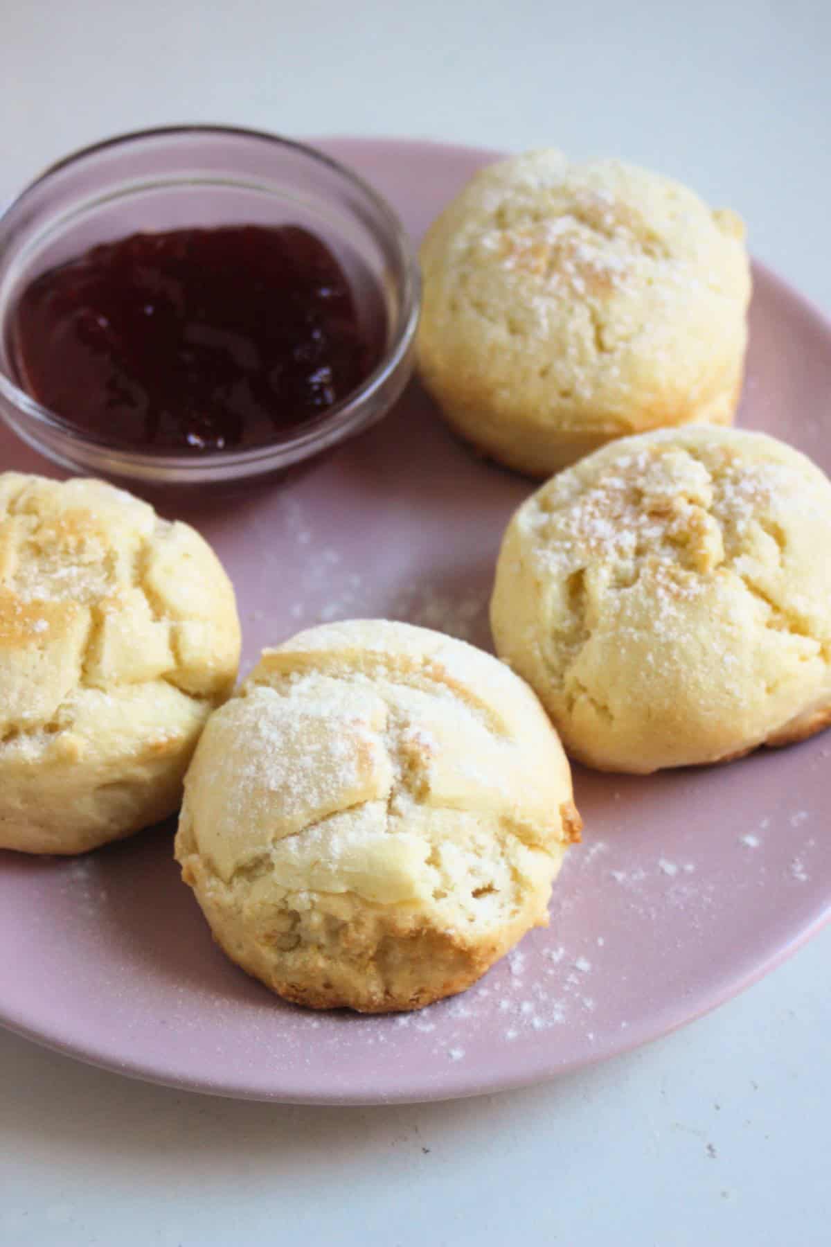 Four scons on a pink plate with a dip of jam.