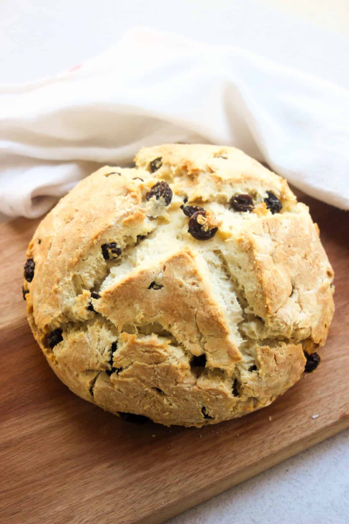 Soda bread with raisins on a wooden board. White kitchen towel behind.