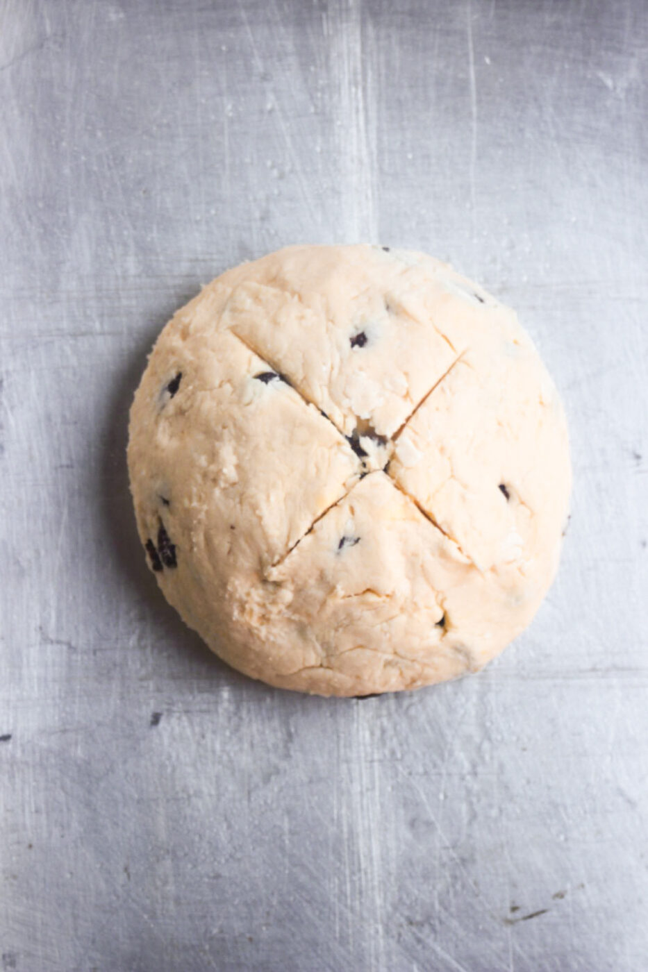 Bread dough shaped round with a cross mark on top on a baking sheet.