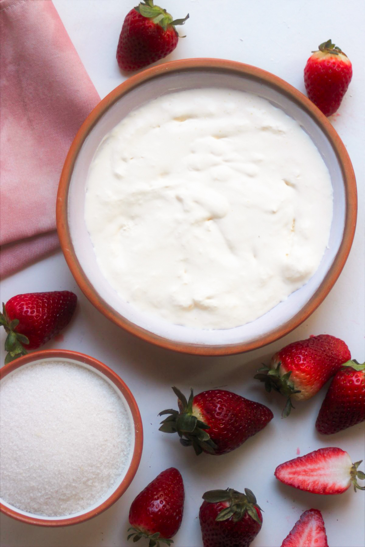 Strawberry Panna Cotta ingredients and a pink napkin on a white surface seen from above.