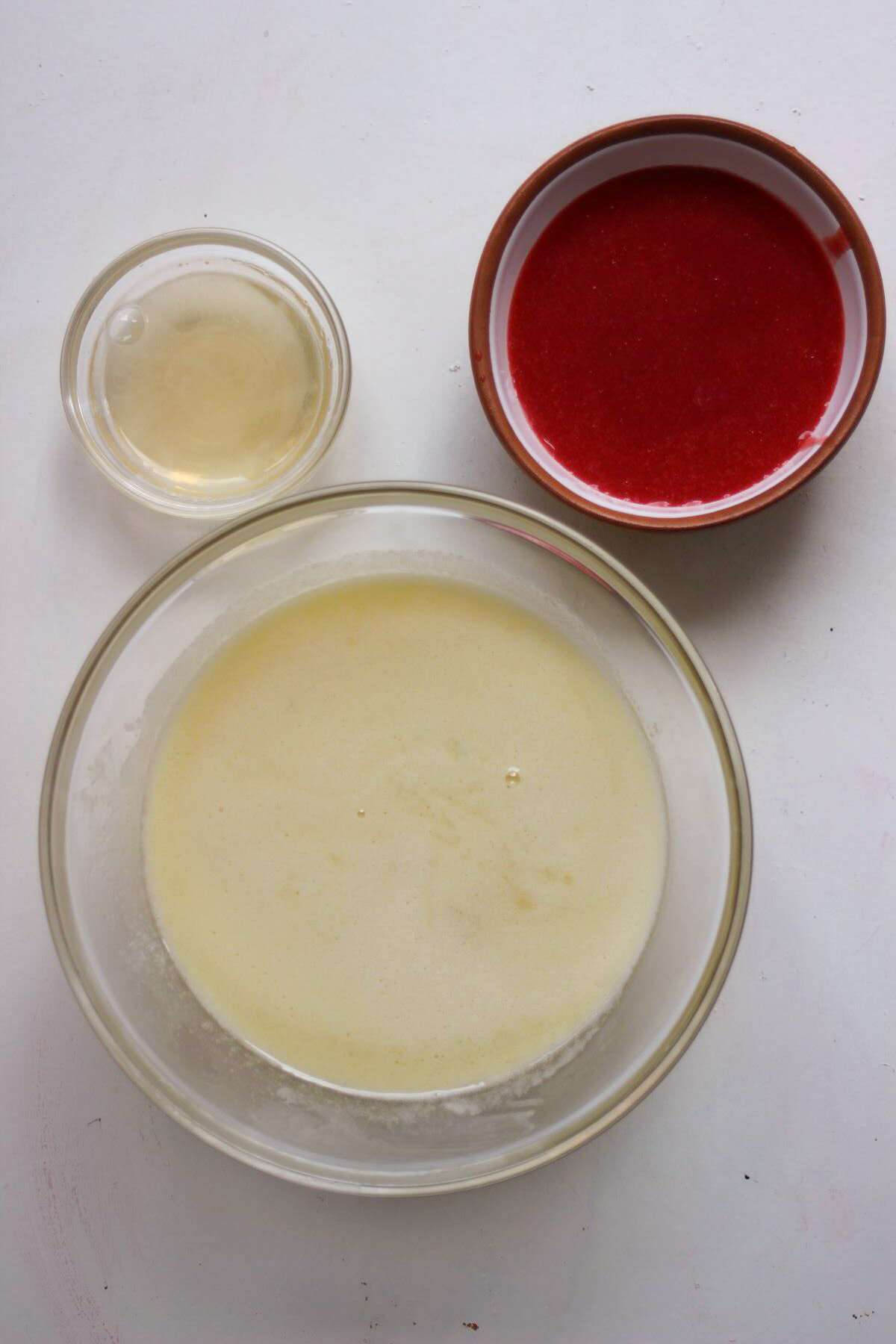Three bowls: one with cream, the other with unflavored gelatin, and the third with strawberry juice.