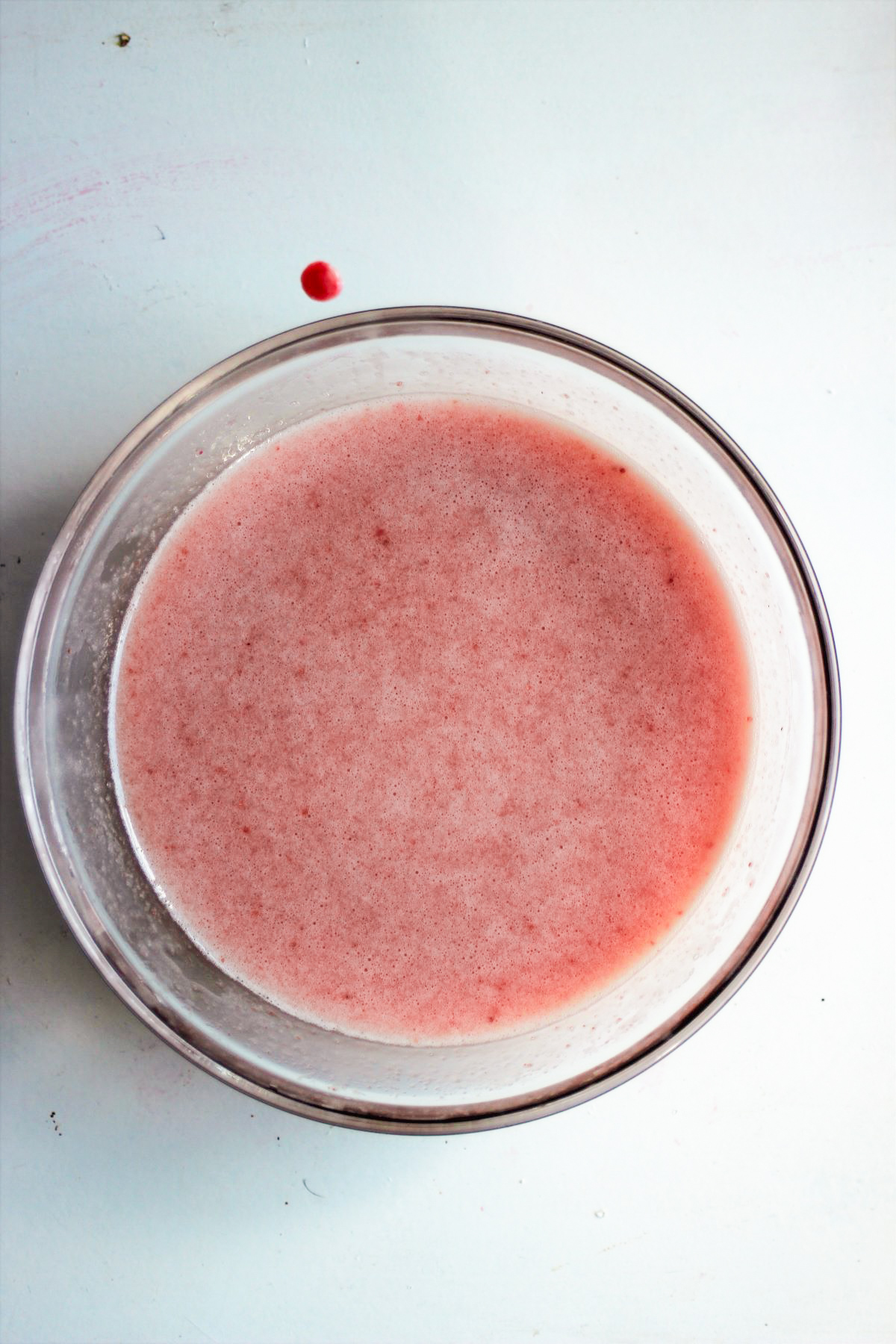 Glass bowl with a pink mixture on a white surface.