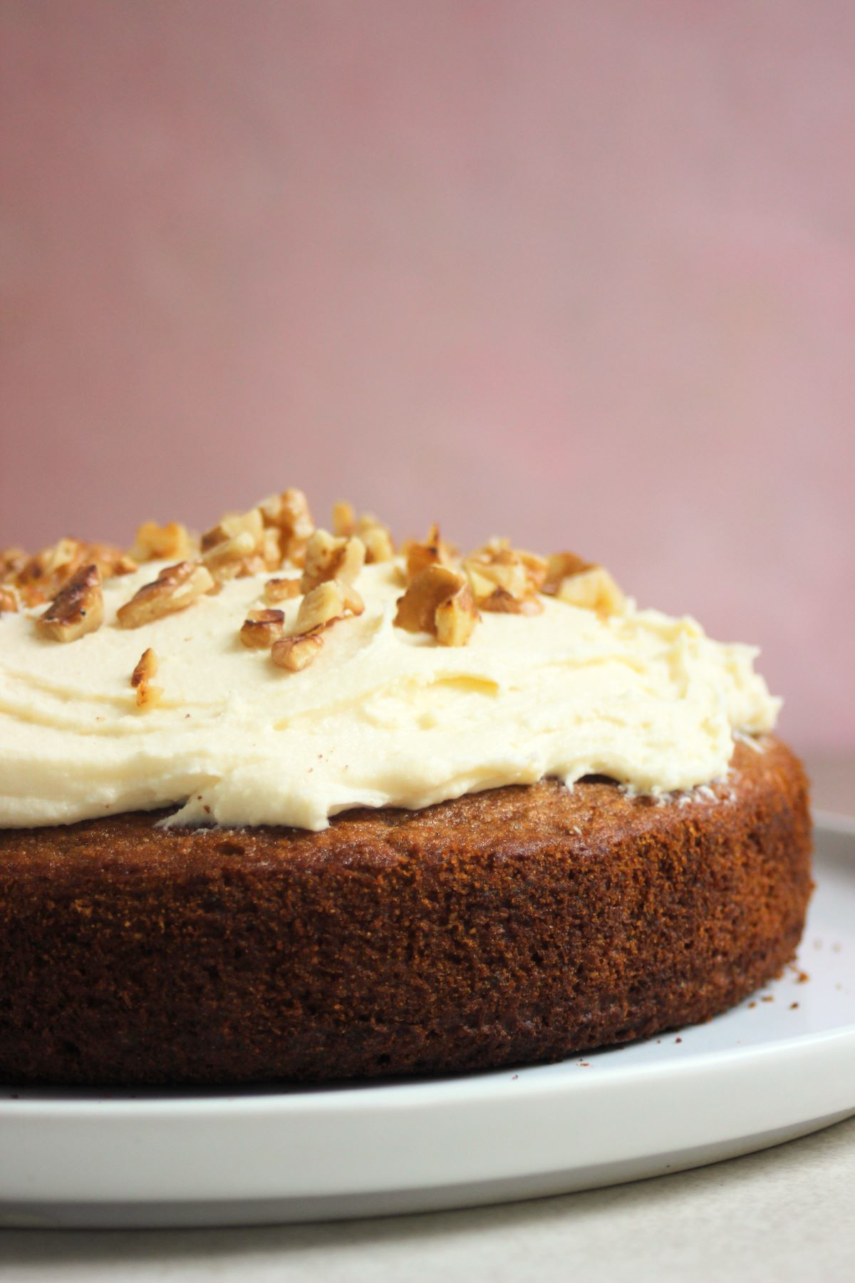 Sweet potato cake with cream cheese frosting and chopped nuts front view on a white plate.
