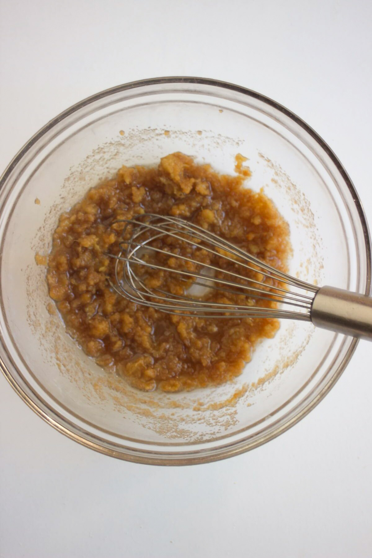 Glass bowl with a brown mixture and a hand whisk.