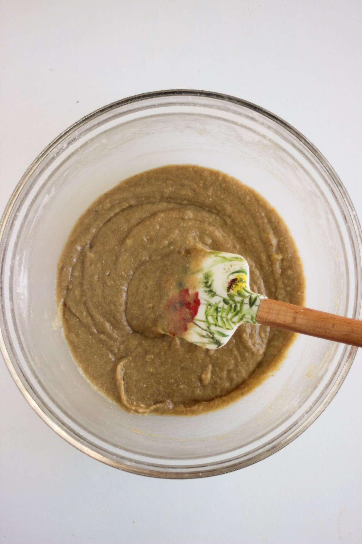 Glass bowl with a smooth brown mixture and a rubber spatula.