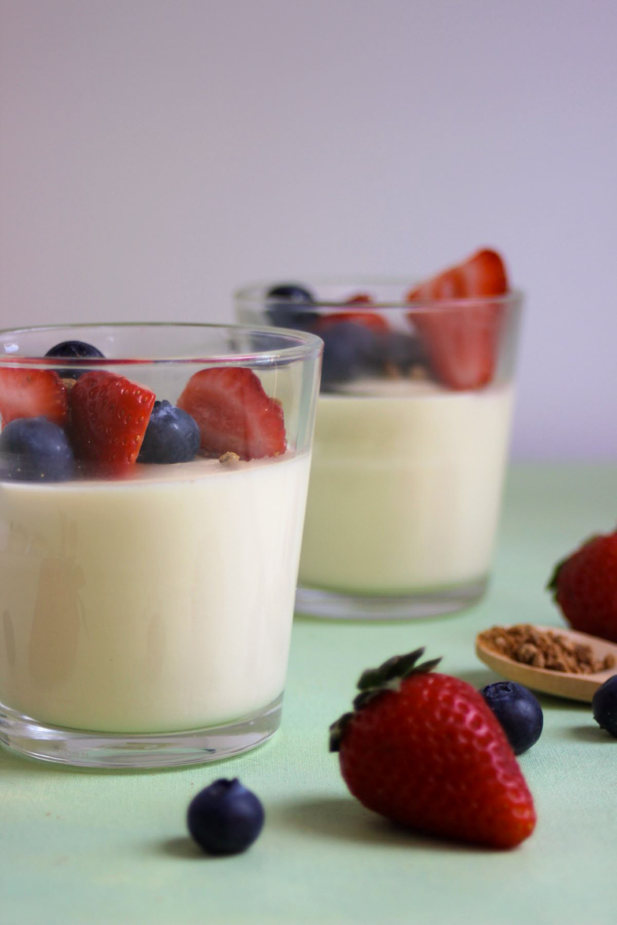 Glass cup with vanilla panna cotta, fresh strawberries, and blueberries. Fresh strawberries and blueberries on the sides.