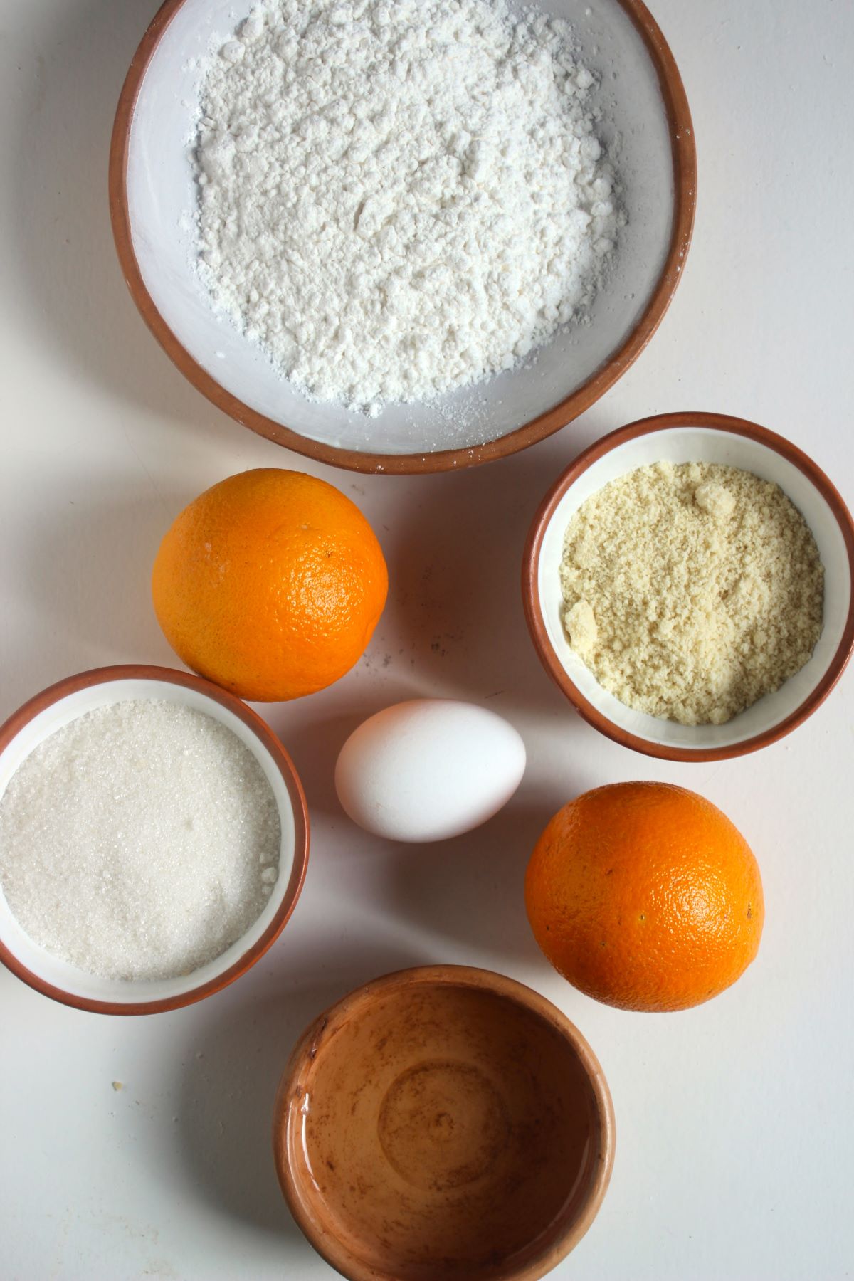 Gluten-free whole orange cake ingredients on a white surface seen from above.