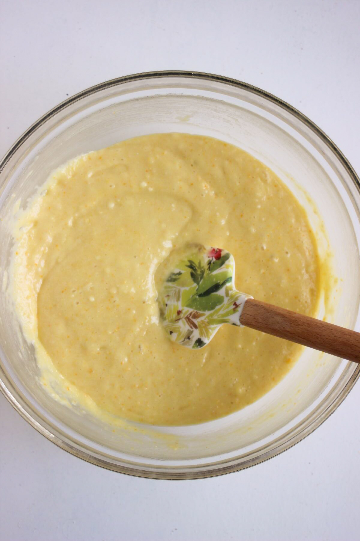 Glass bowl with a light yellow mixture and a rubber spatula.