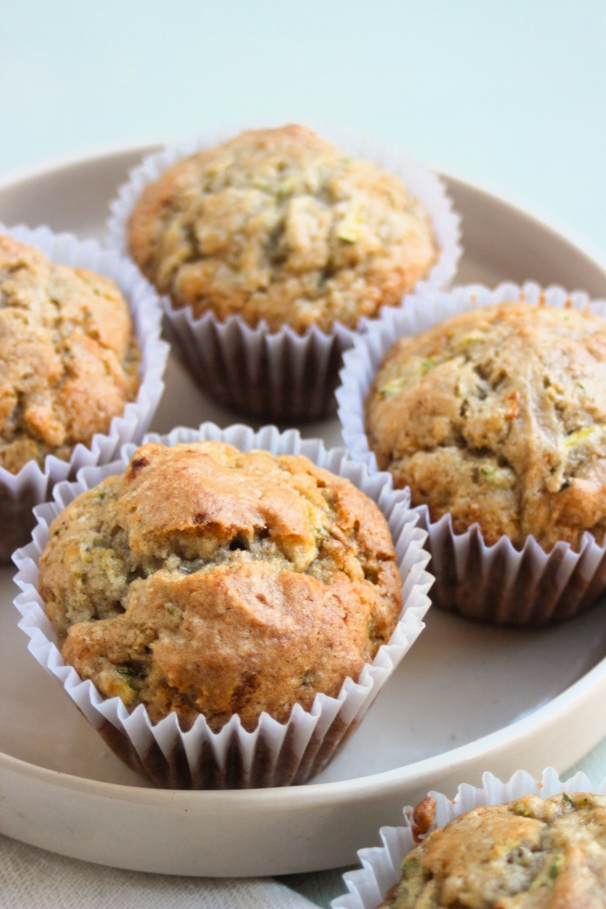 Zucchini muffins with liners on a cream color plate.