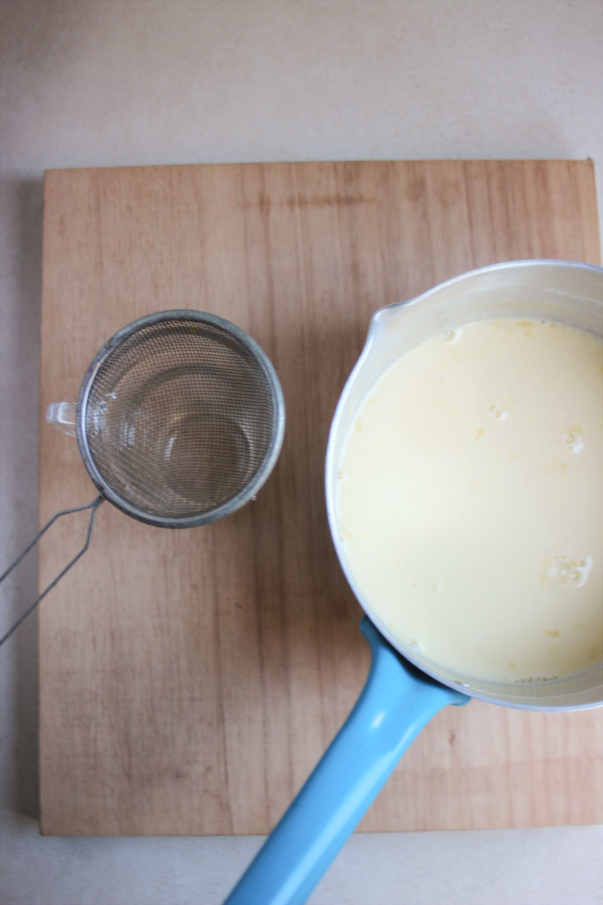 Saucepan with milk, a strainer on the side, on a wooden board.
