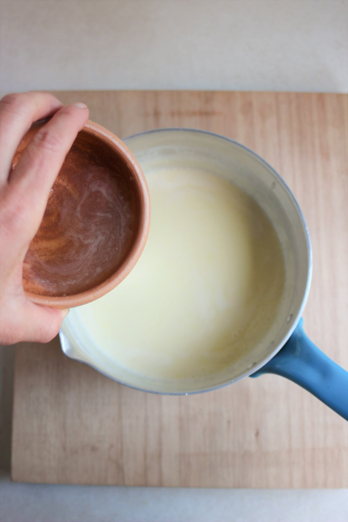 Tiny bowl with a liquid is about to be poured into a saucepan with milk.