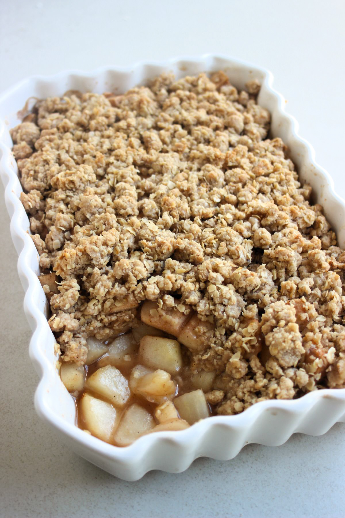 Rectangular baking dish with pear crisp. One part is not complete, and there are chopped pears with juice.