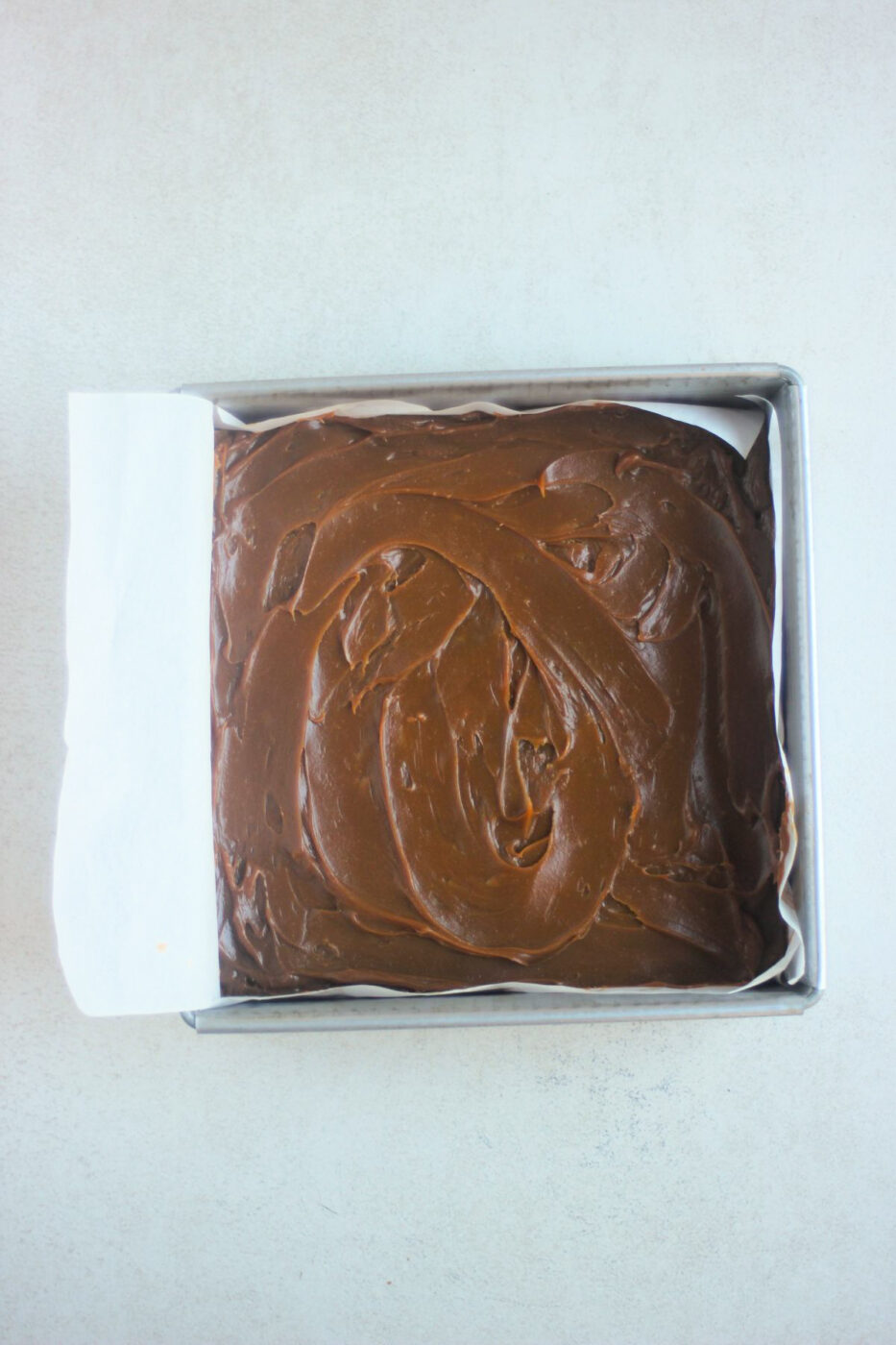 Top view of a square baking pan with parchment paper and dulce de leche.