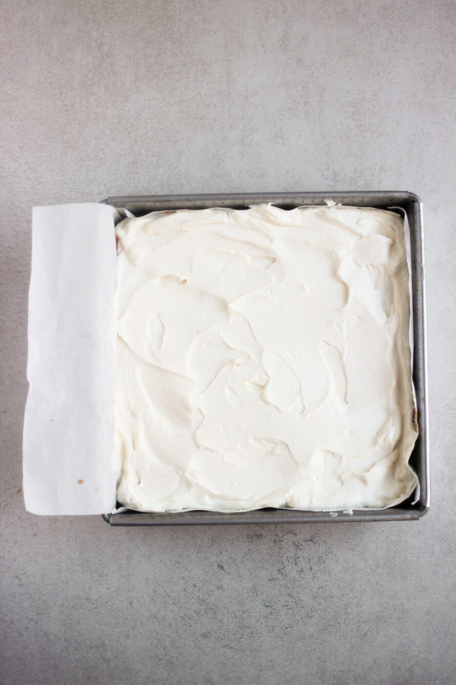 Top view of a square baking pan with parchment paper and whipped cream.