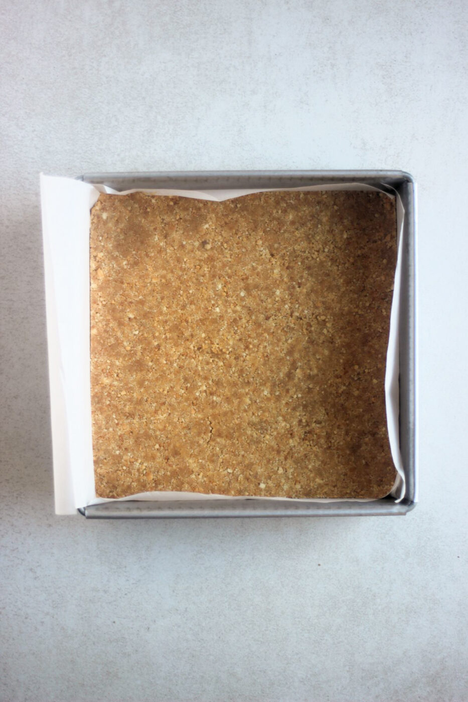 Top view of a square baking pan with parchment paper and cookie crust.
