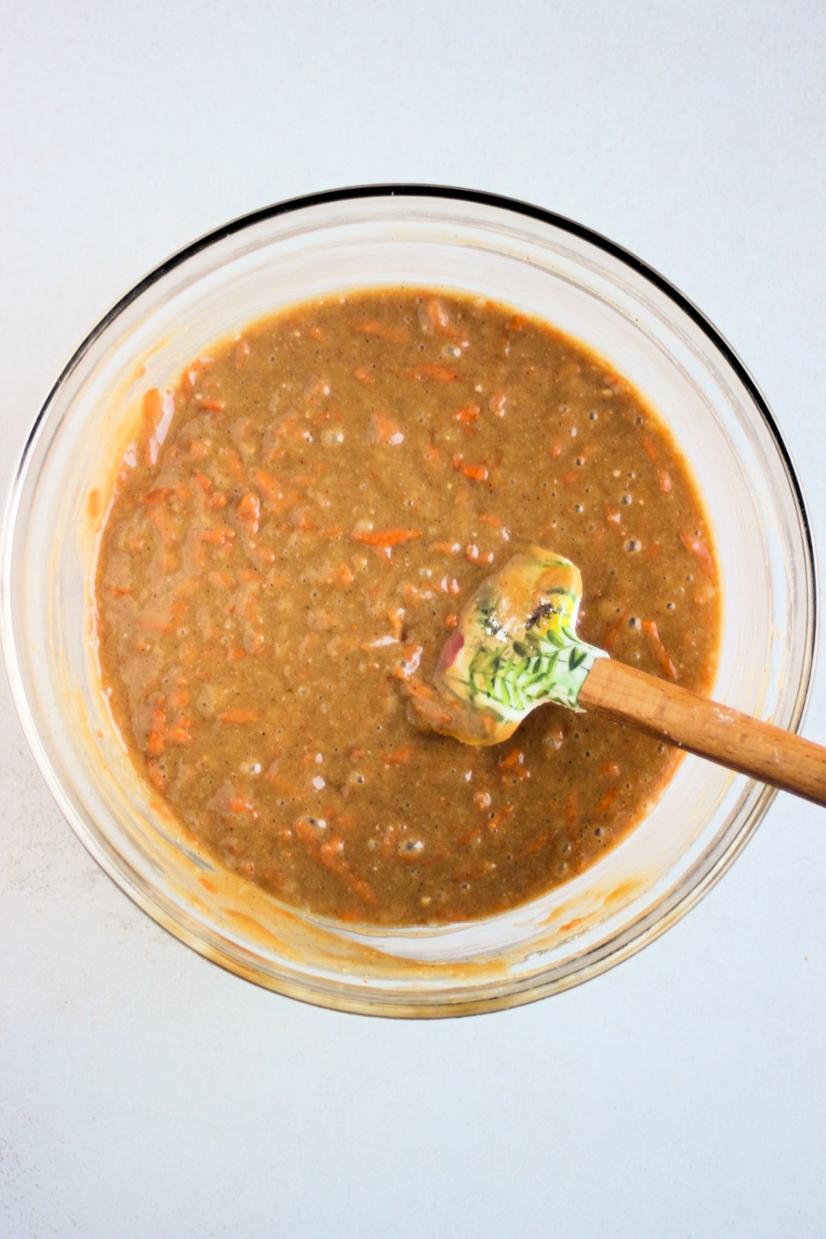 Glass bowl with carrot laof cake batter and a rubber spatula.