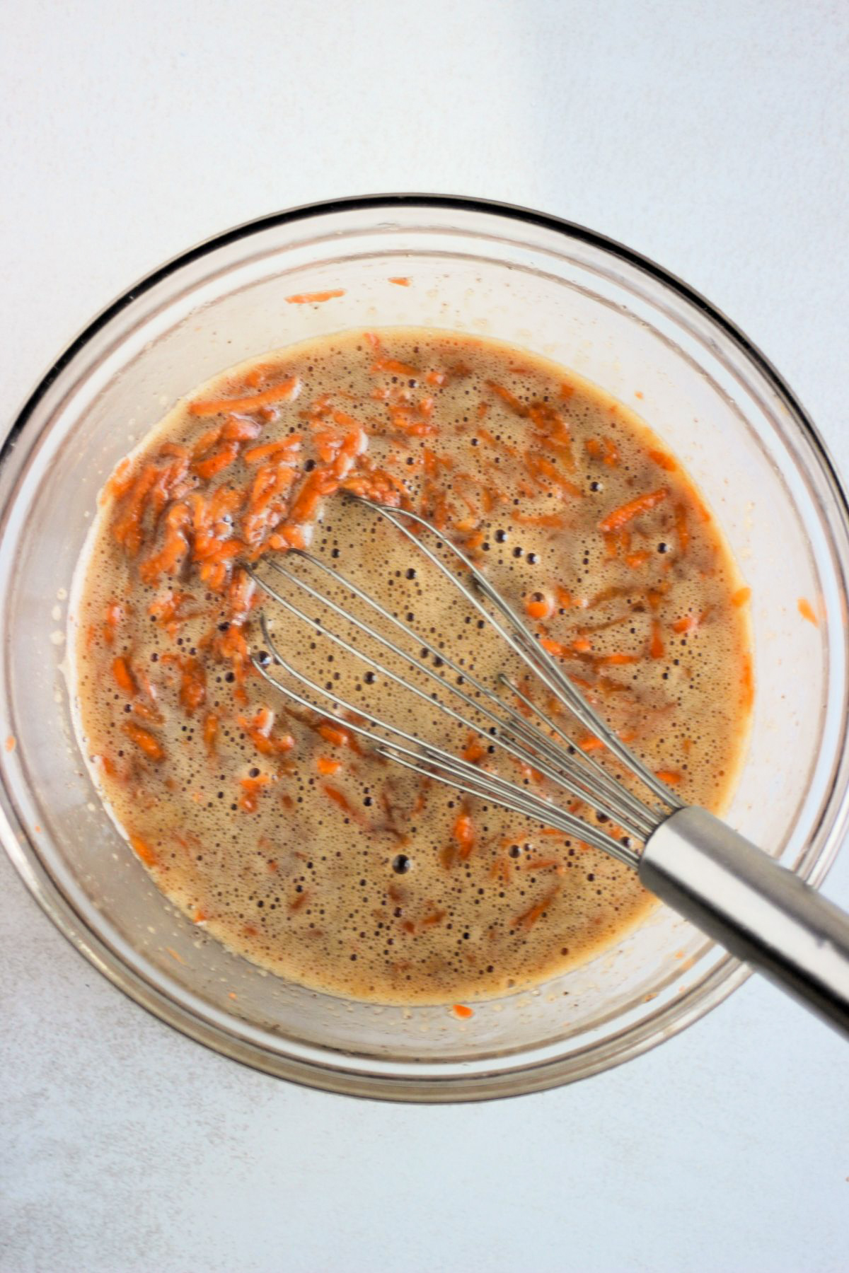 Glass bowl with carrot laof cake mixtureand a hand whisk.