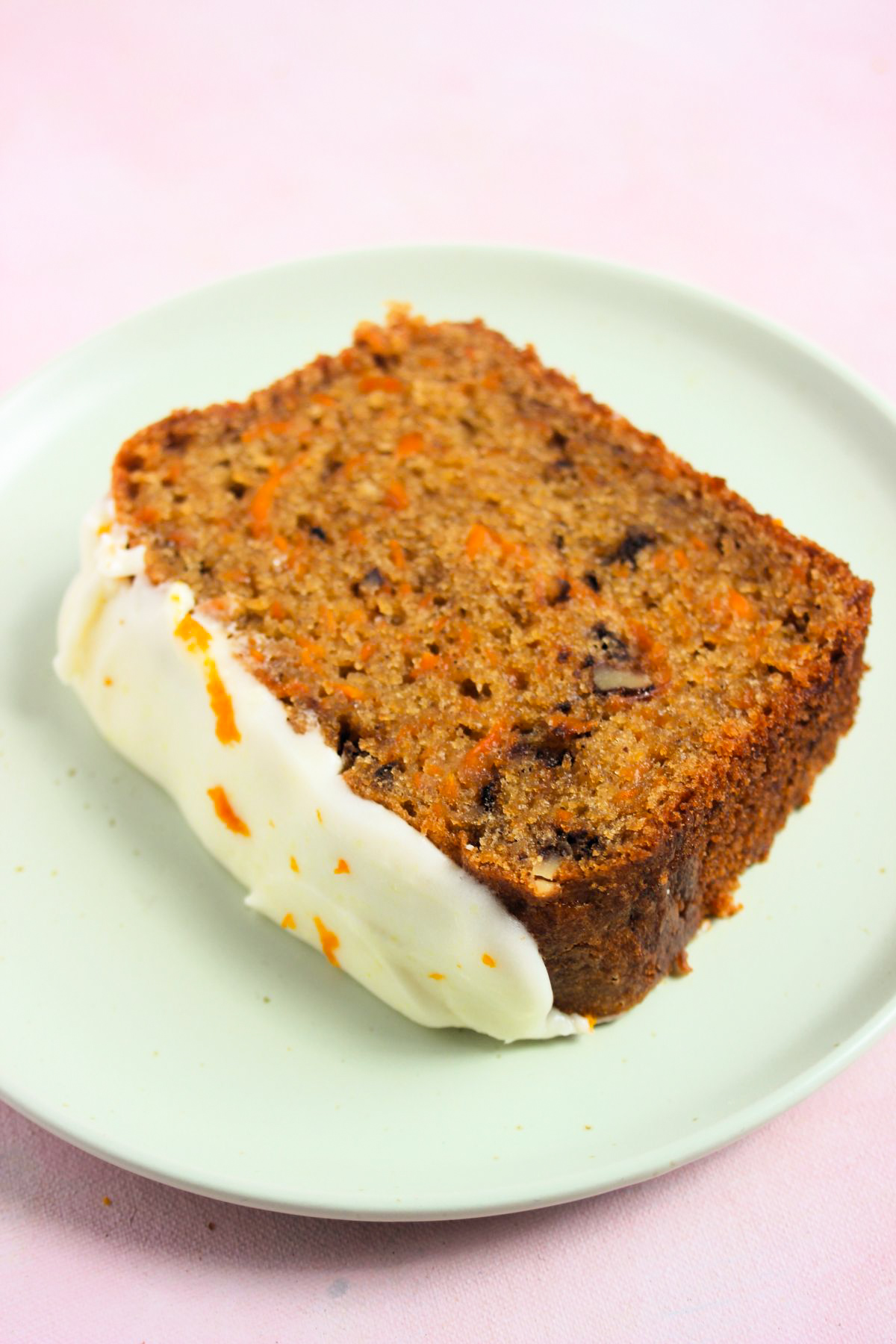 A slice of carrot loaf cake with cream cheese frosting on an aqua-green plate.