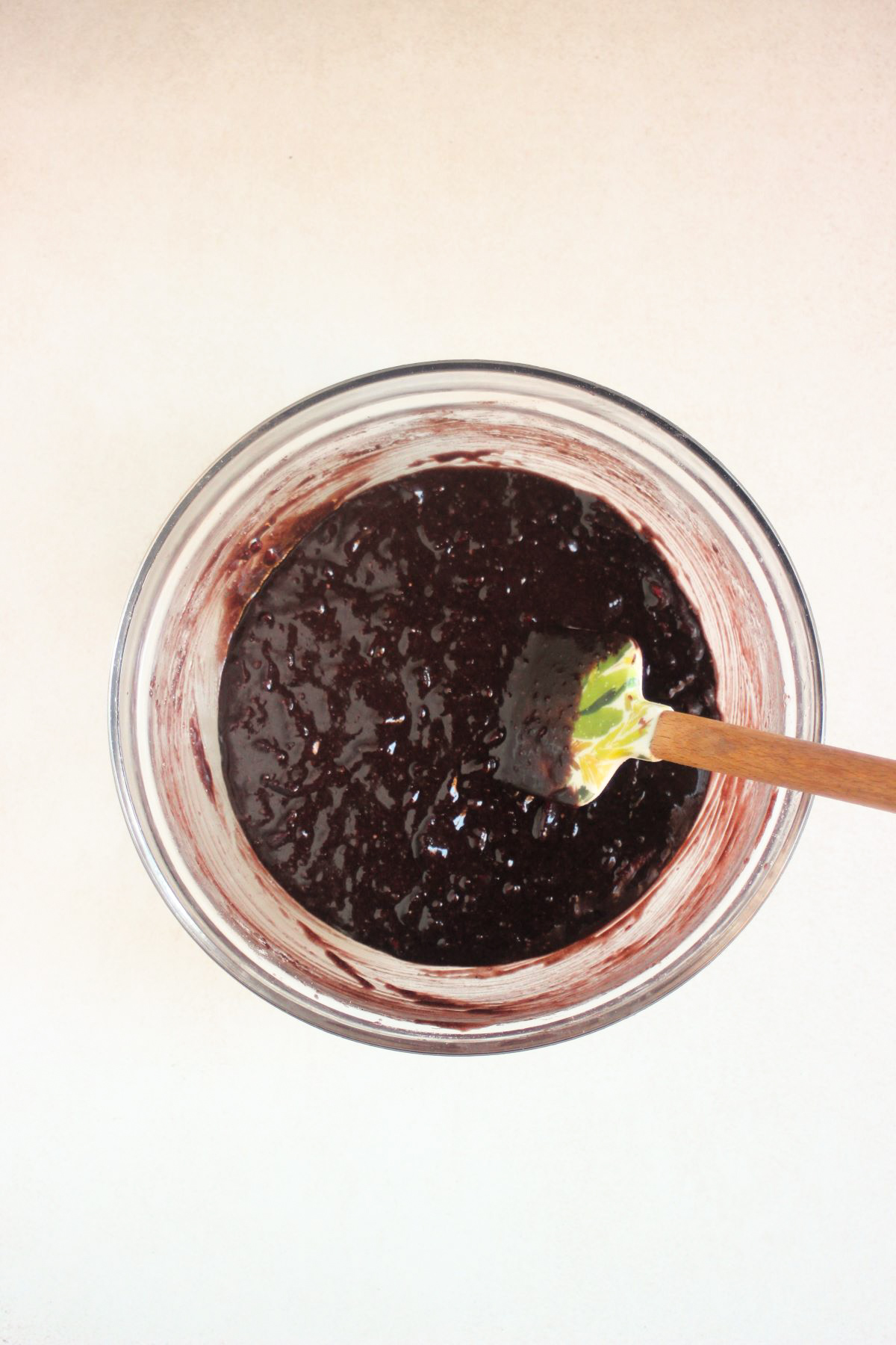 Glass bowl with a brown thick mixture and a rubber spatula.