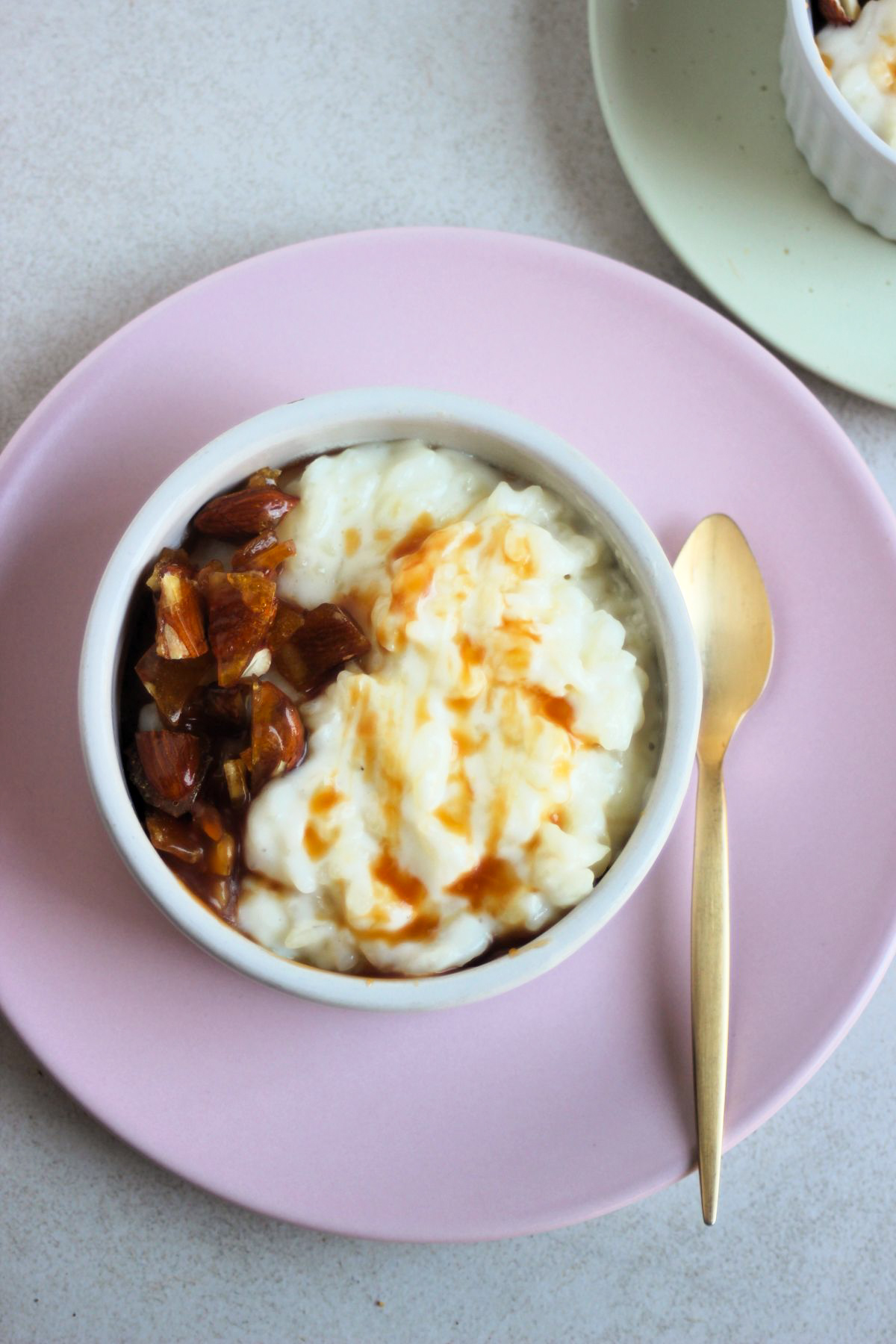 Top view of a small bowl with rice pudding, caramel, and praline on a pink plate.