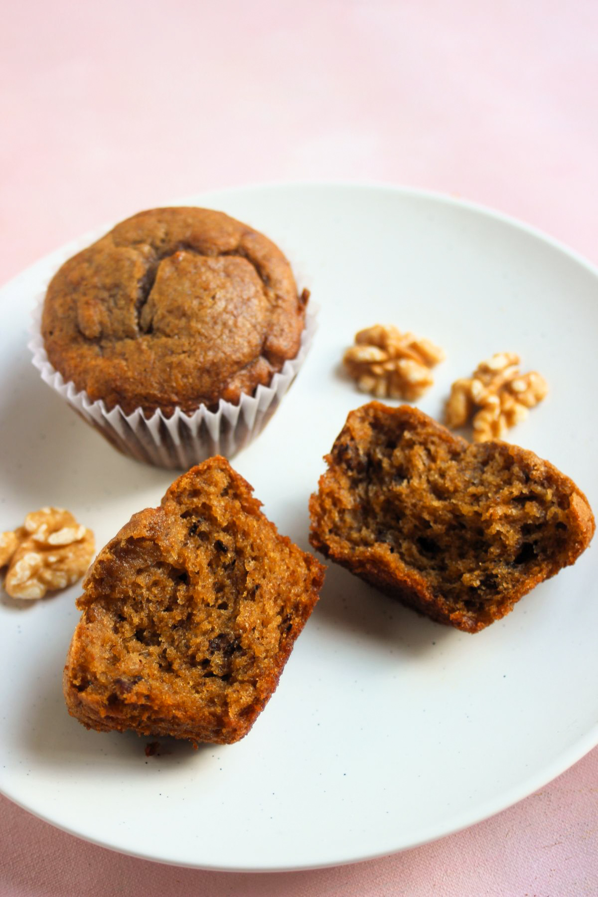 Sweet potato muffin with liner and another muffin cut in half on a white plate.