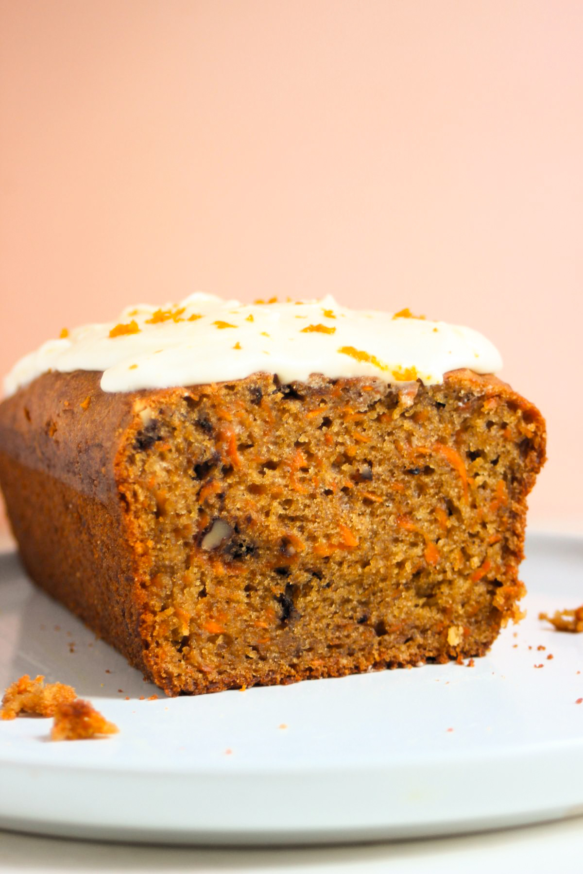 Front view on carrot loaf cake with cream cheese frosting. Light orange background.