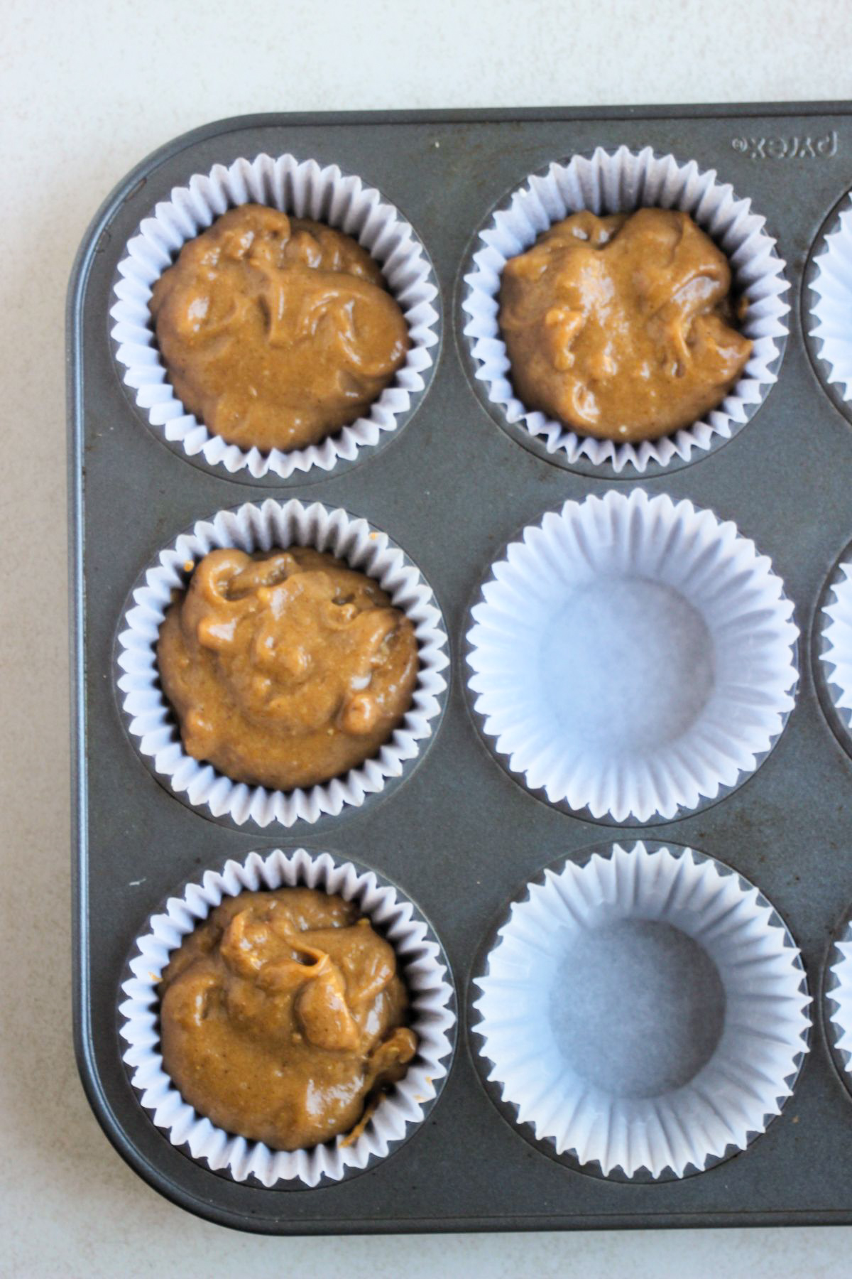 Top view of a muffin pan with liners, some filled with sweet potato batter.