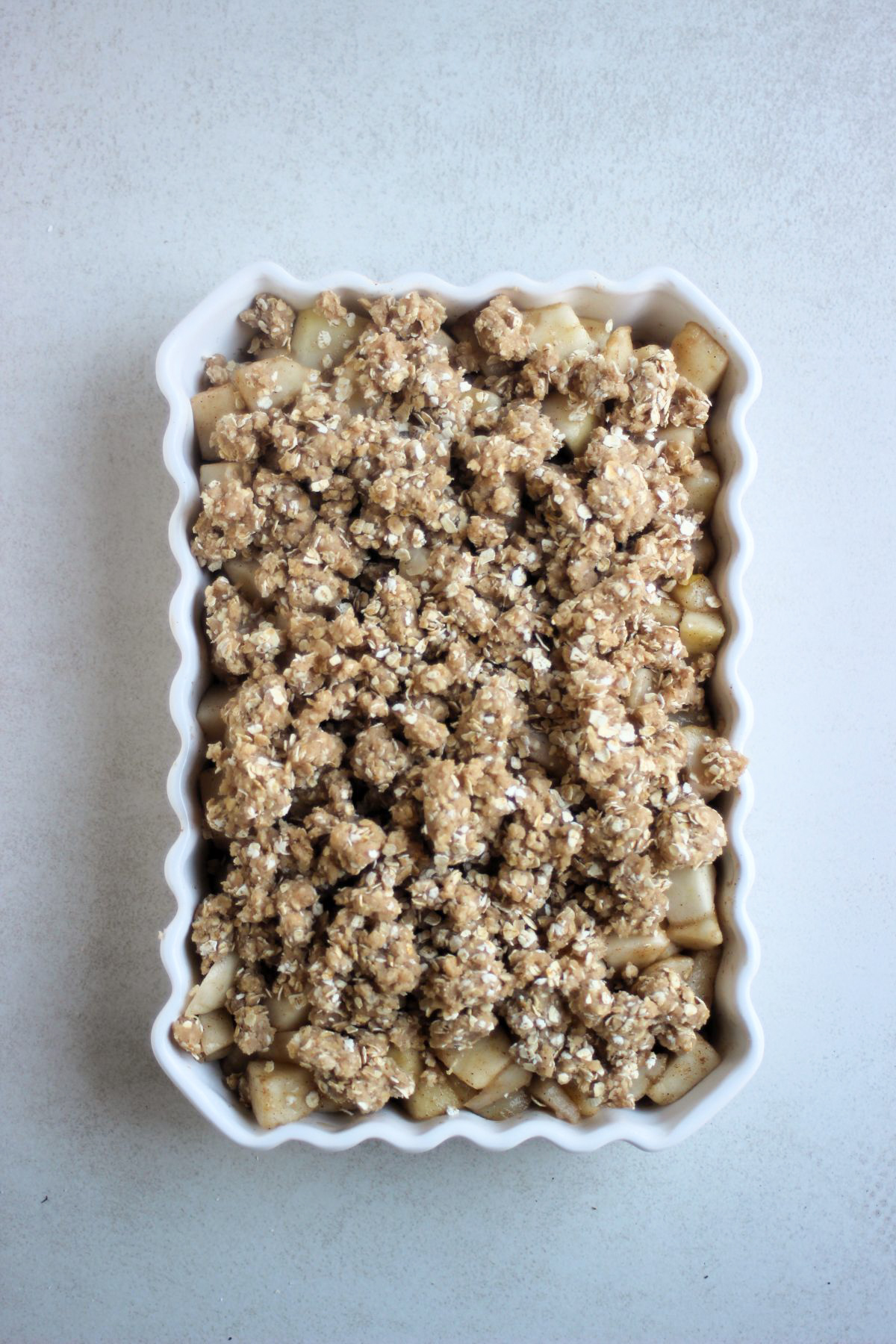 Rectangular baking dish with raw pear crisp seen from above.