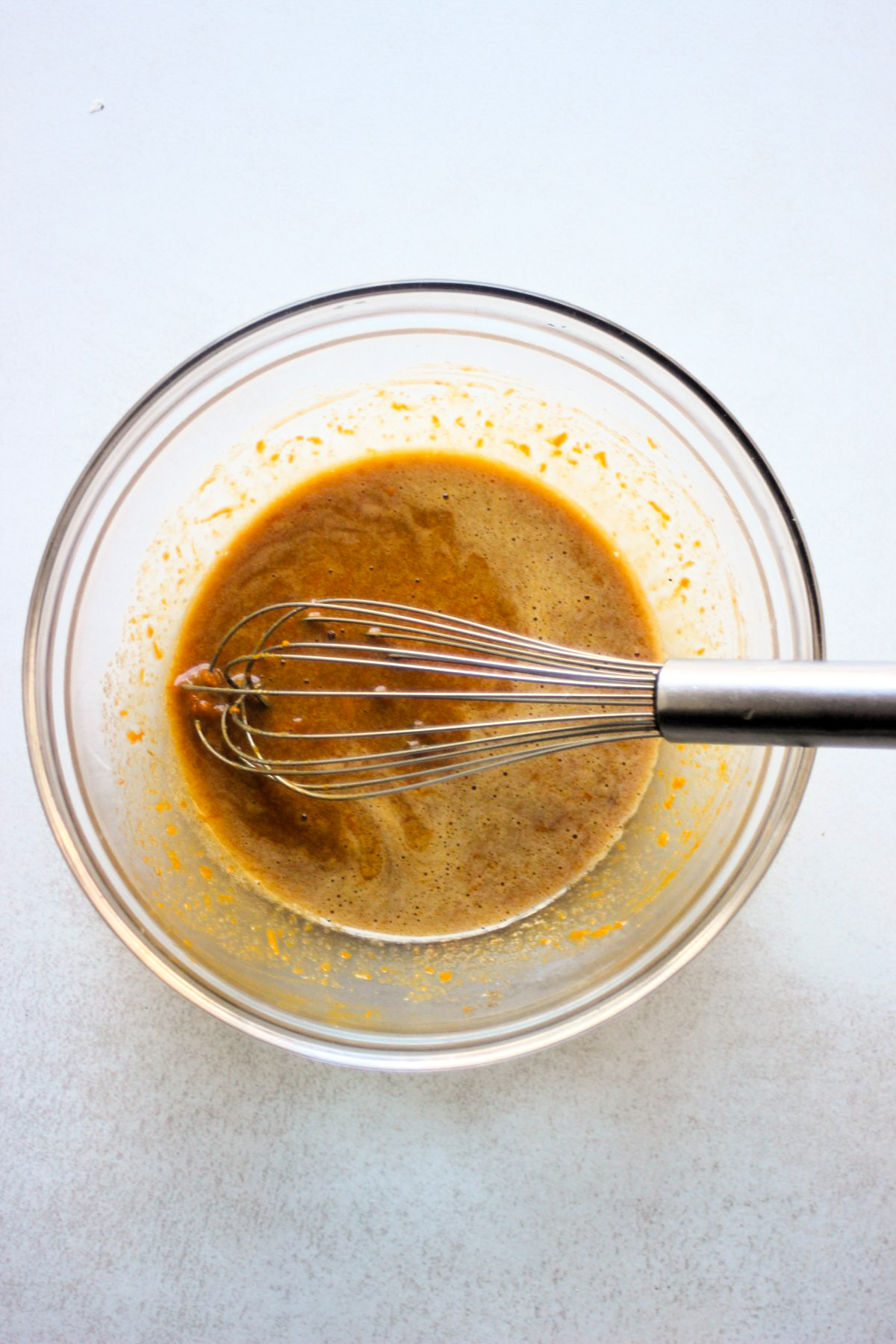 Glass bowl with an orange liquid and a hand whisk.