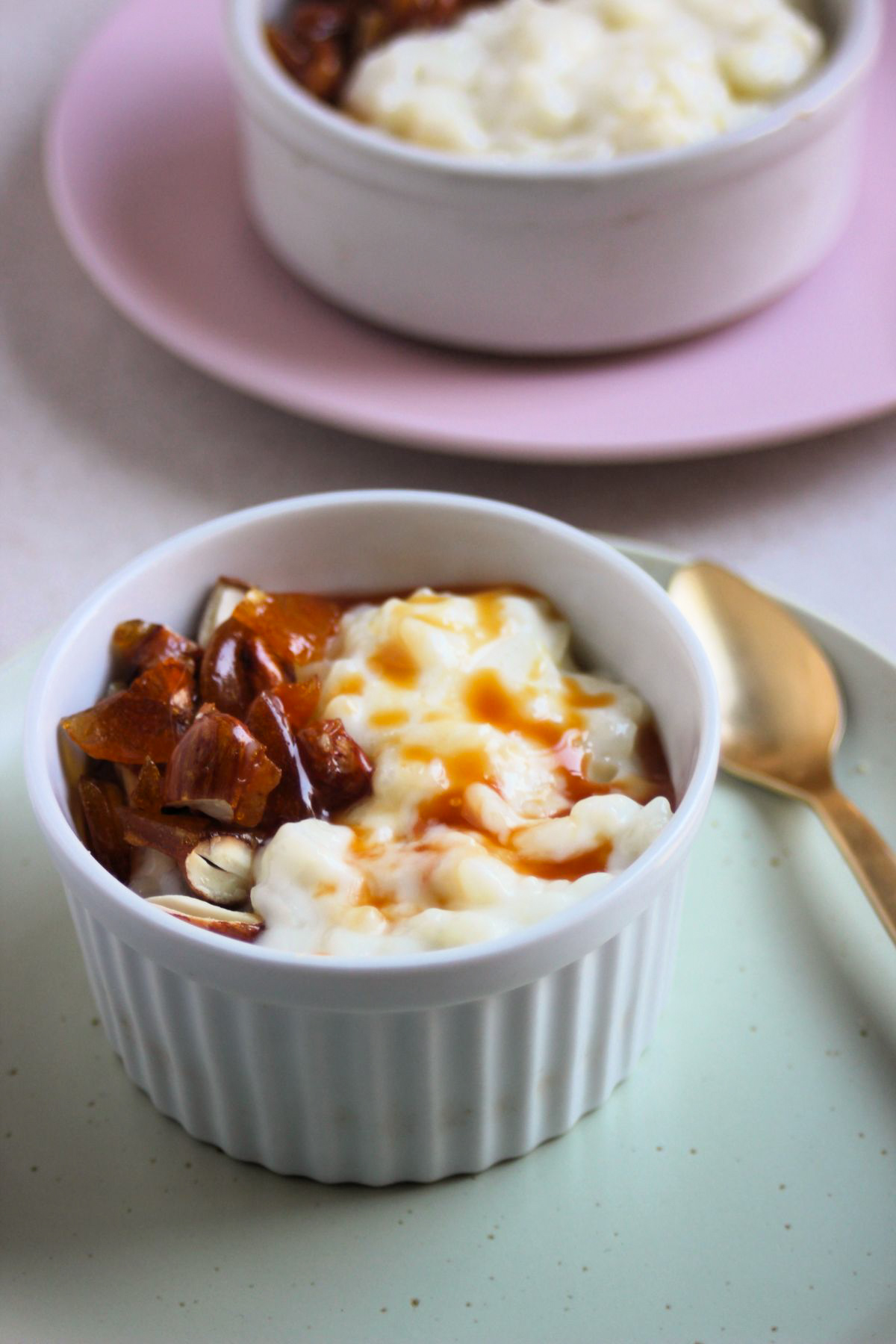 Small bowl with rice pudding, caramel, and praline on an aqua green plate.