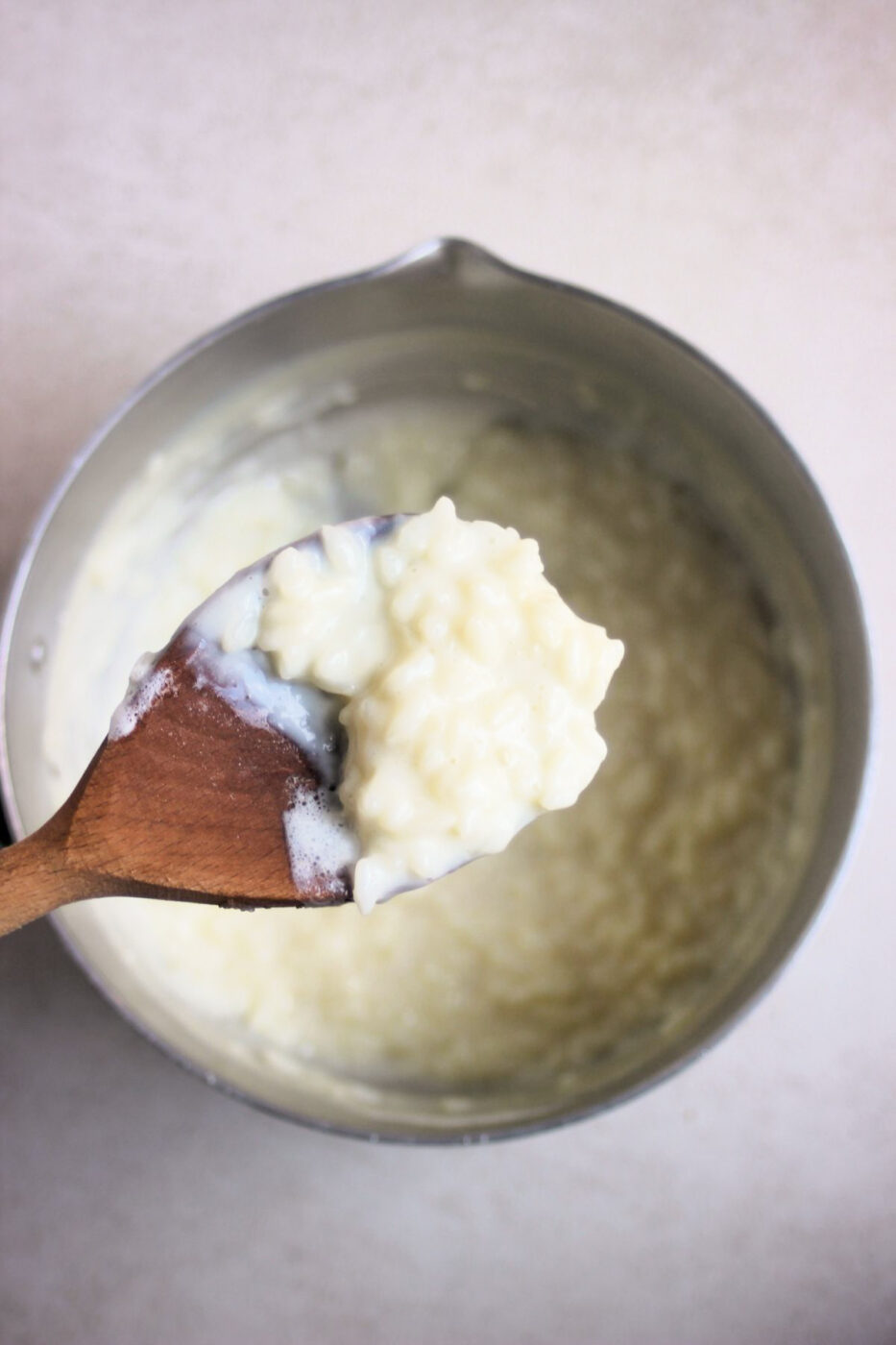 Wooden spoon with rice pudding in the foreground. Behind it, a deep pan with rice pudding.