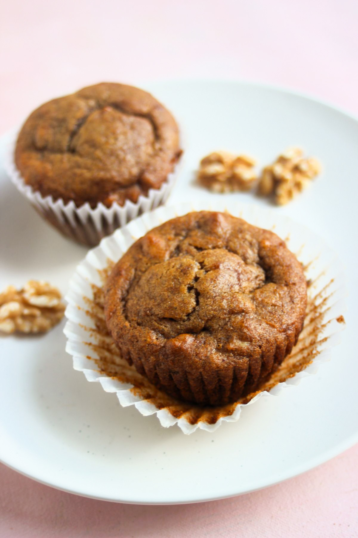 Two sweet potato muffins on a white plate and walnuts around.