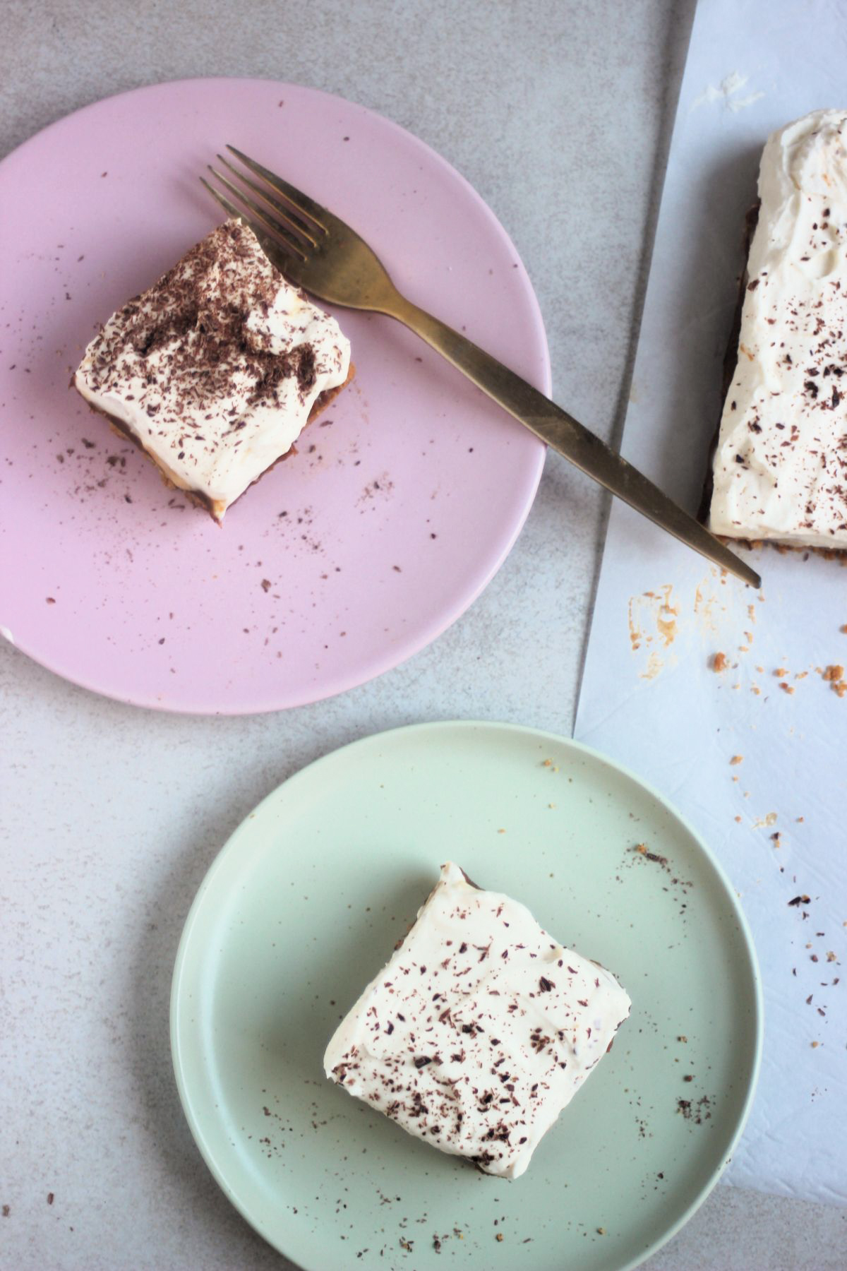Top view of a pink plate with a banoffee pie bar and a golden fork, and an aqua-green plate with a banoffee pie bar.