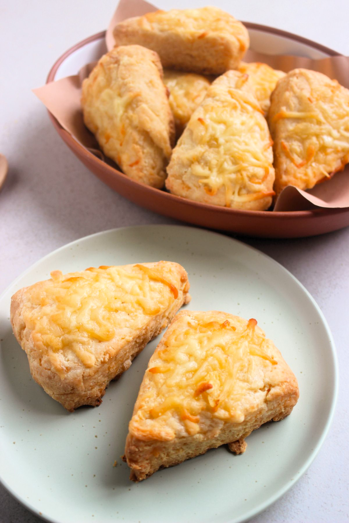Two cheese scones on a plate and more scones behind on a deep dish.