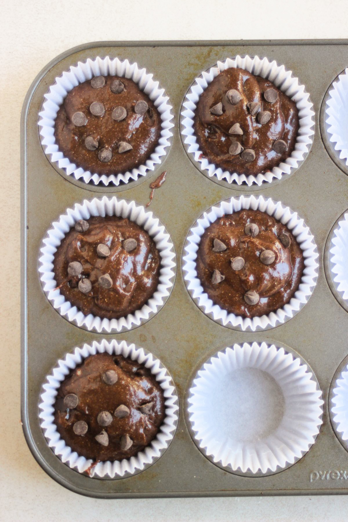 Baking pan with liners filled with chocolate buckwheat muffin batter.
