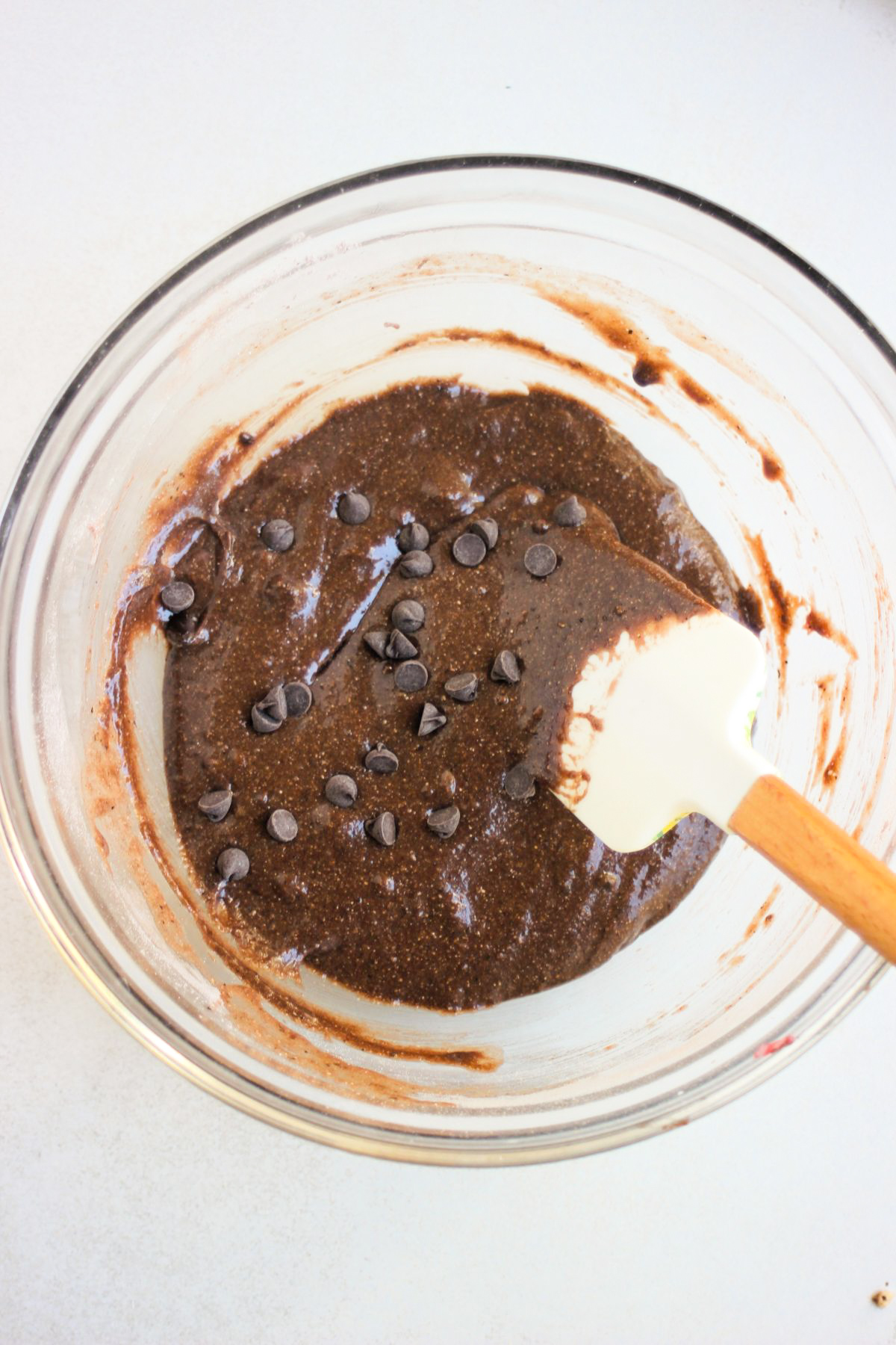 Glass bowl with chocolate buckwheat muffin batter and a rubber spatula.