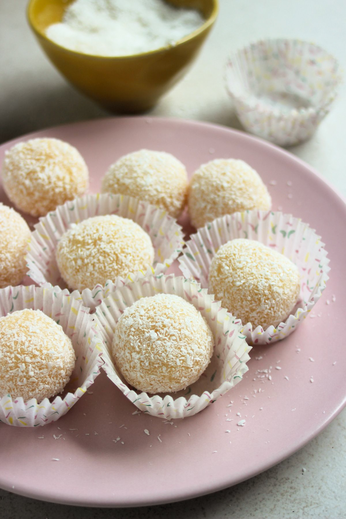 Coconut brigadeiros in liners on a pink plate.