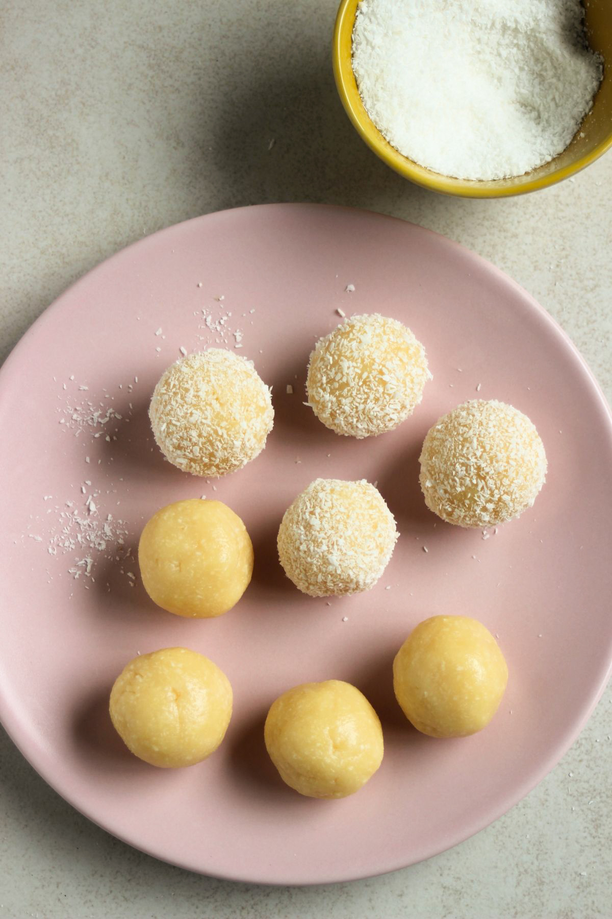 Top view of coconut brigadeiros on a pink plate, some rolled in shredded coconut.