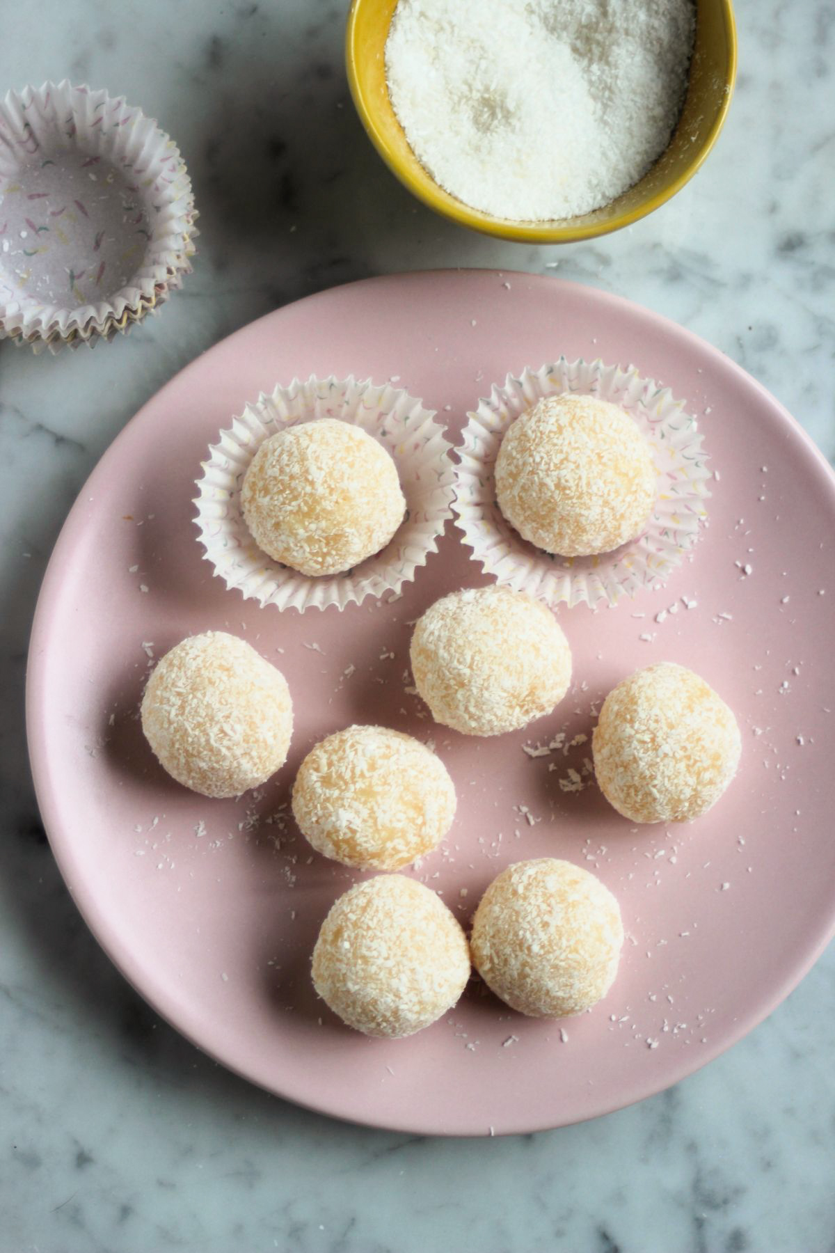 Top view of coconut brigadeiros on a pink plate, some in liners.