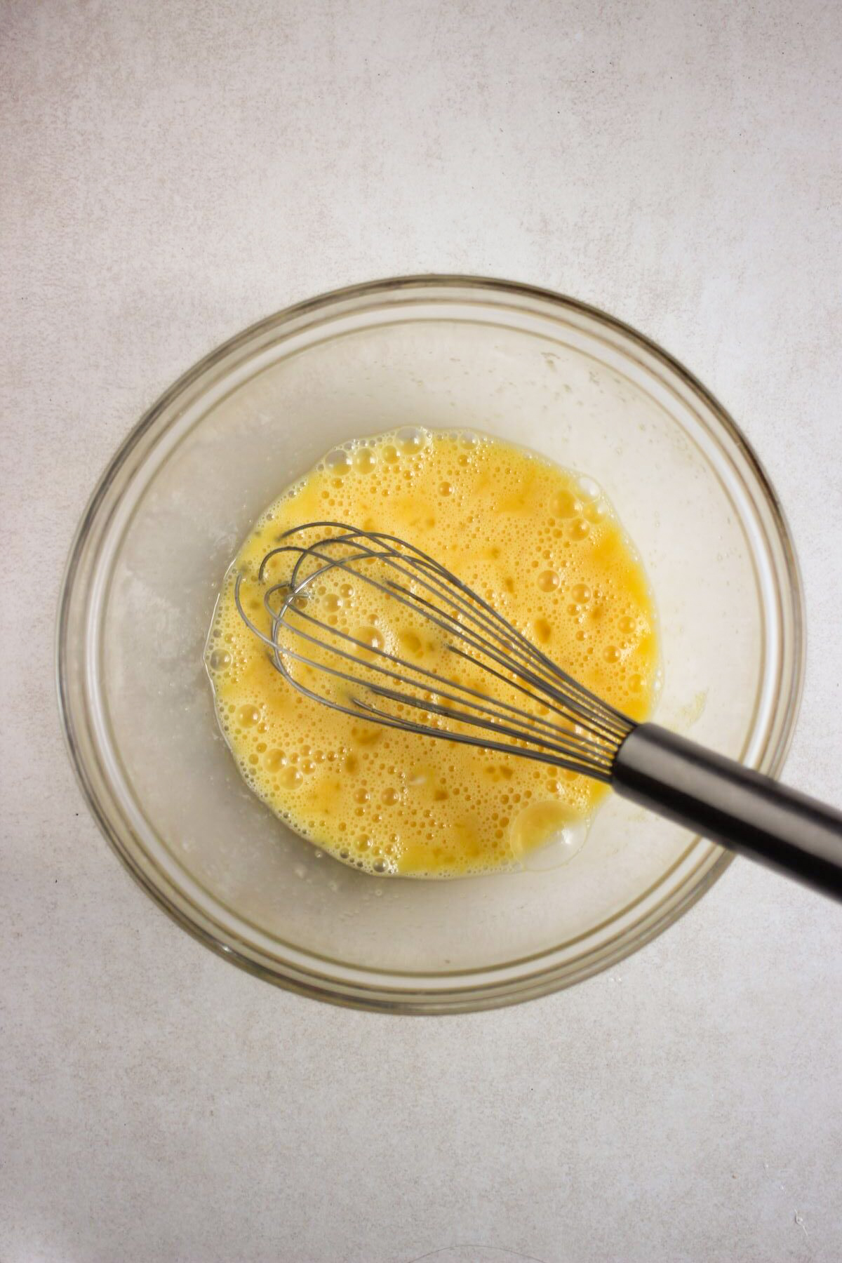 Glass bowl with an egg mixture and a hand whisk.