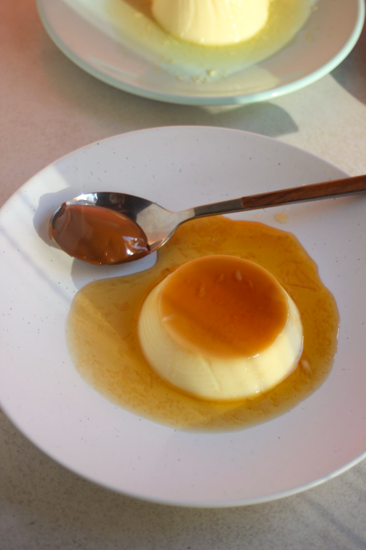 Flan with caramel and a spoon with dulce de leche on a white plate.