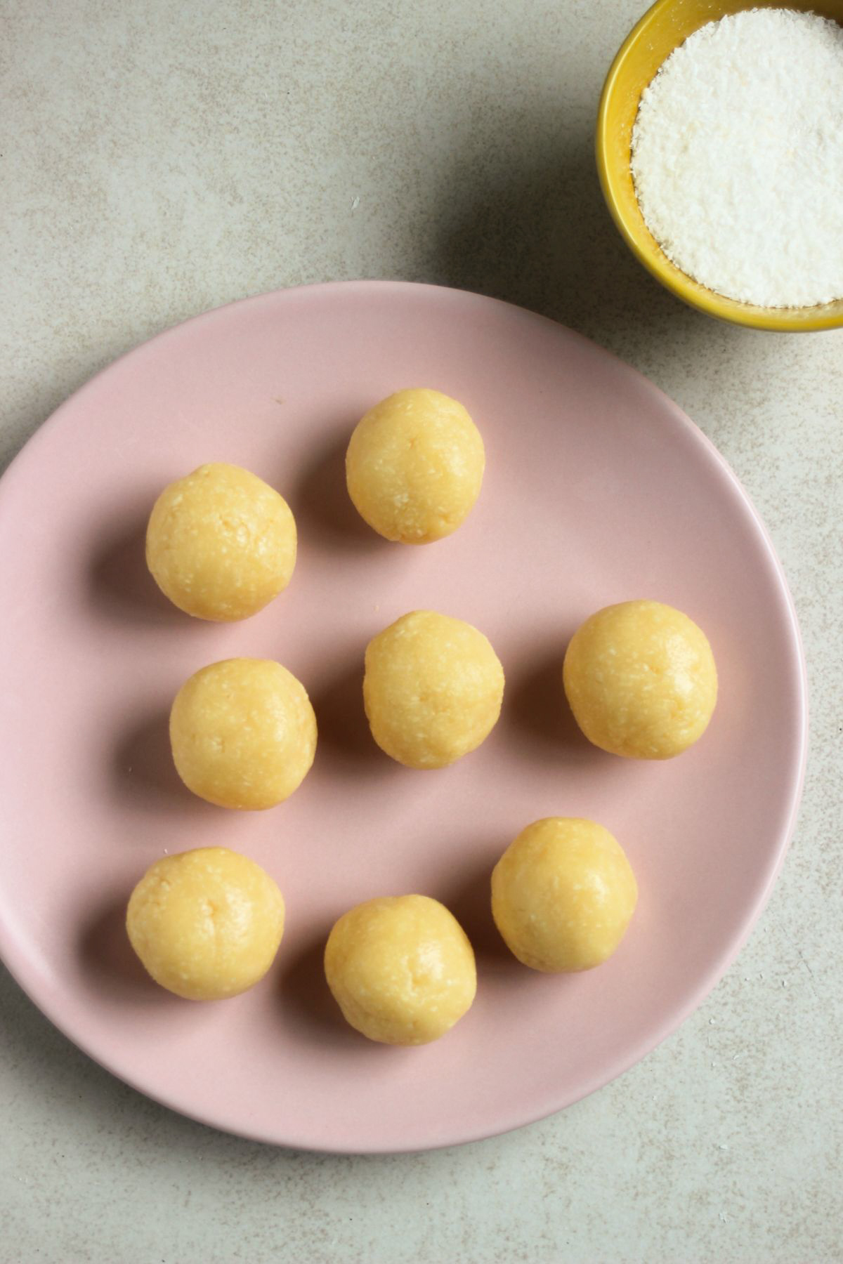Top view of coconut brigadeiros on a pink plate without being rolled in shredded coconut.